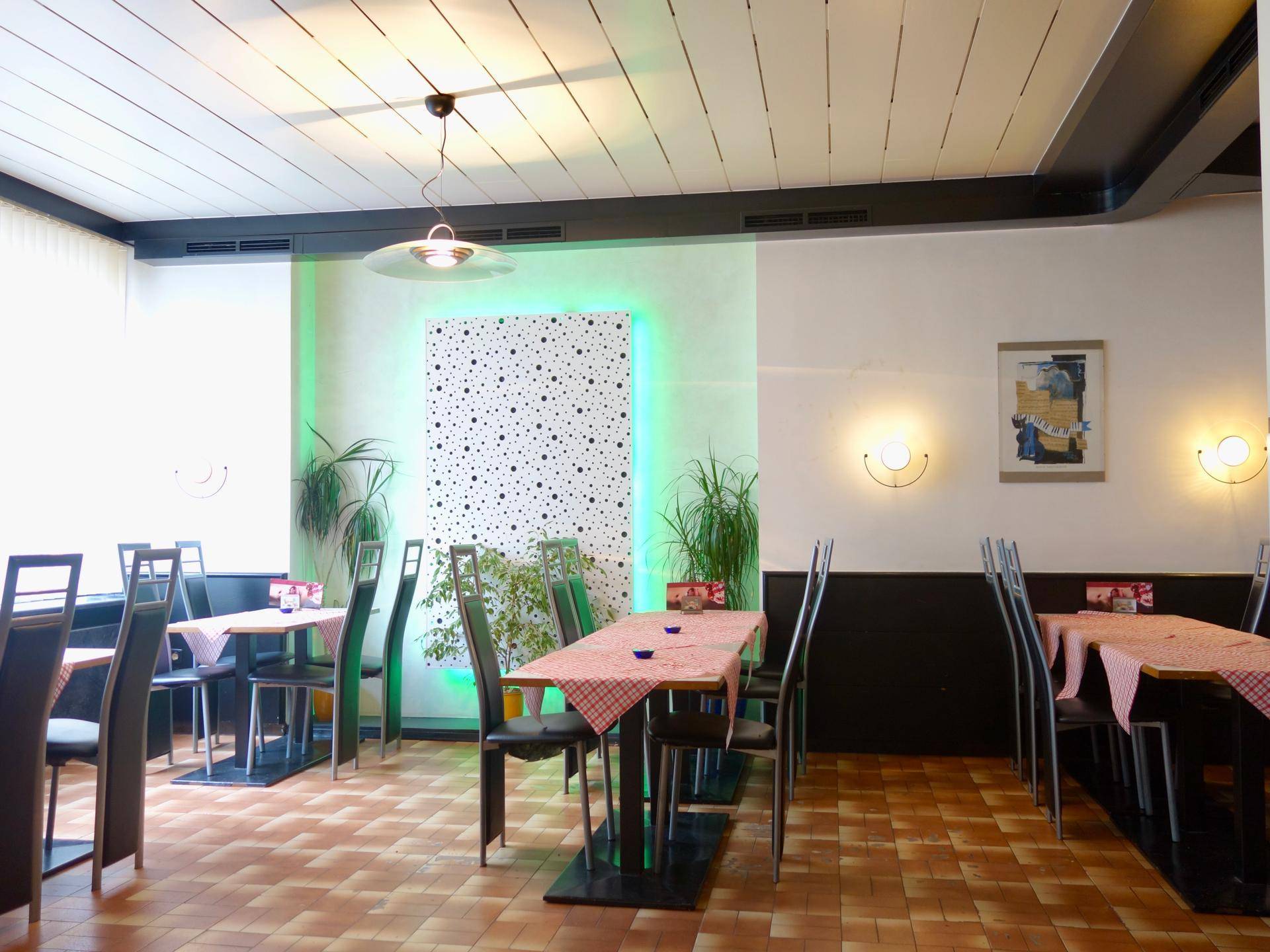 Restaurantbereich mit Tischen, Stühlen und einer Wanddekoration mit grüner Beleuchtung.