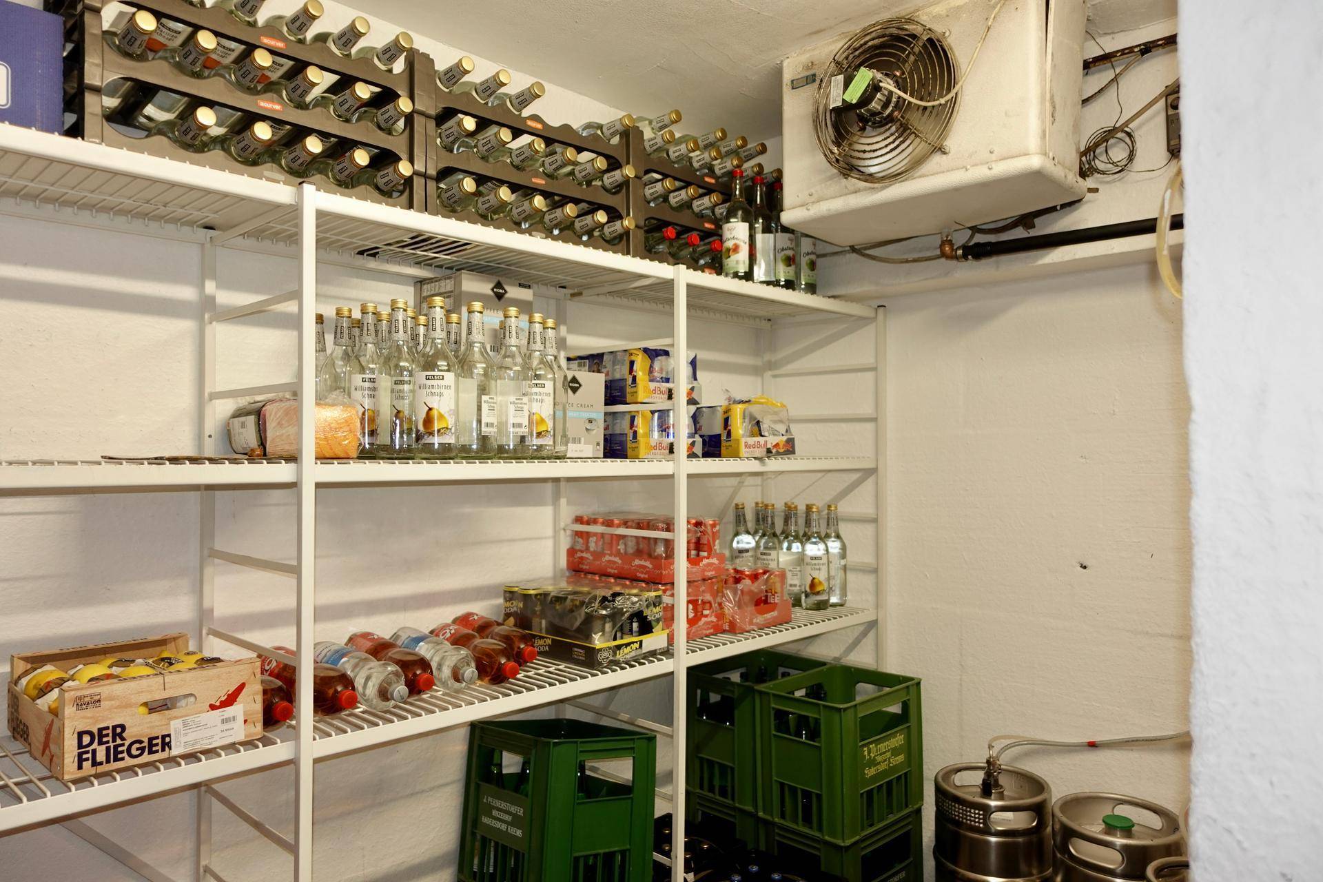 Ein Kühlraum mit Regalen voller Getränke und Weinflaschen, ausgestattet mit einer Kühlanlage an der Decke.