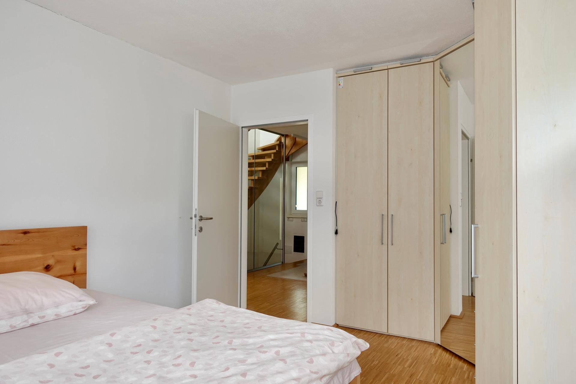 Gemütliches Schlafzimmer mit Holzbettrahmen, Einbauschränken und Blick zum Treppenhaus.