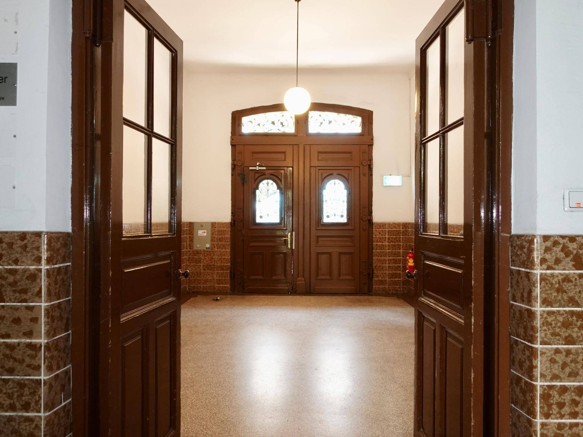Eingangsbereich mit großen, verzierten Holztüren, Fliesenboden und einem klassischen Ambiente.