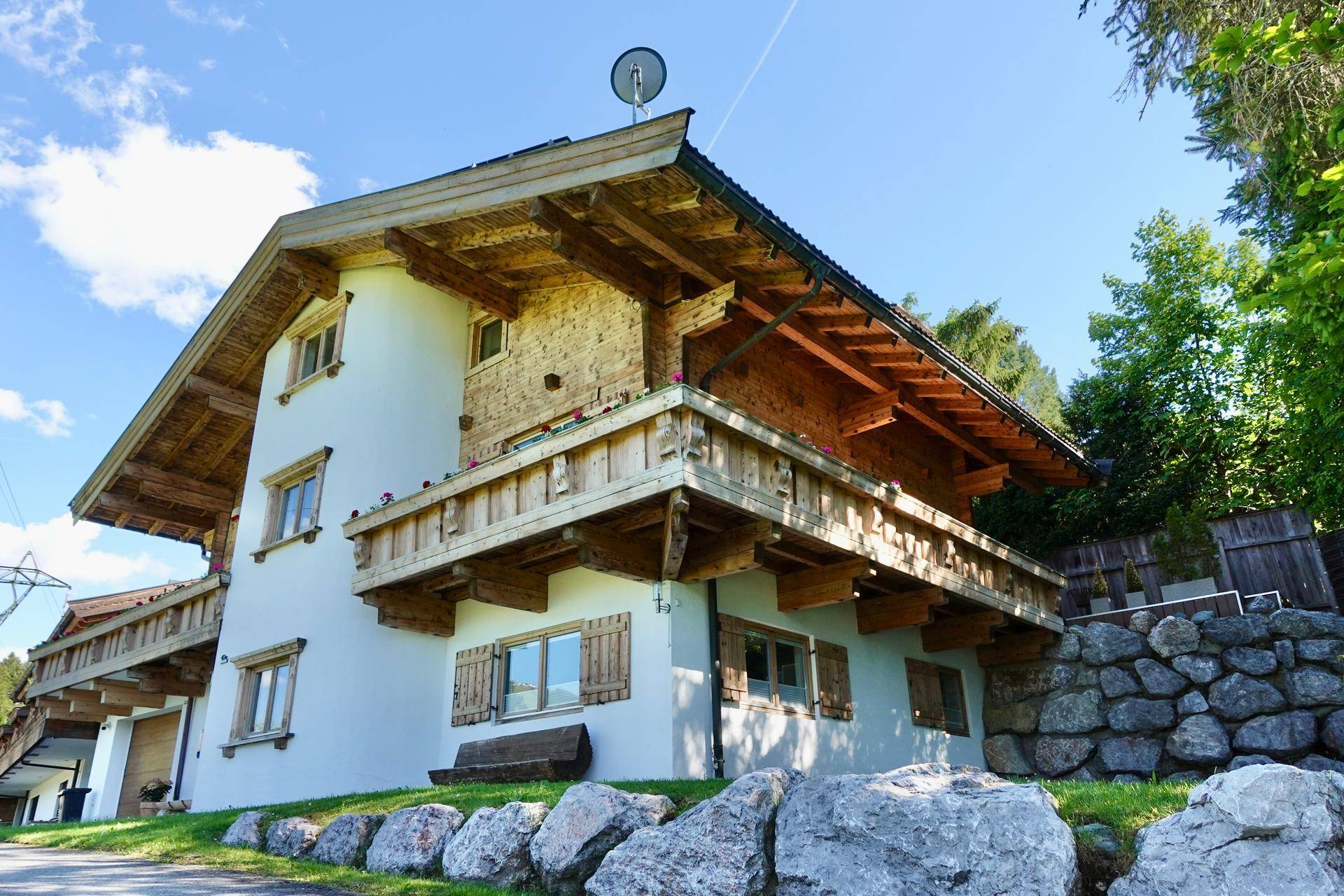 Charmantes Holzhaus mit weißer Fassade und traditionellen Balkonen, eingebettet in eine grüne Landschaft.