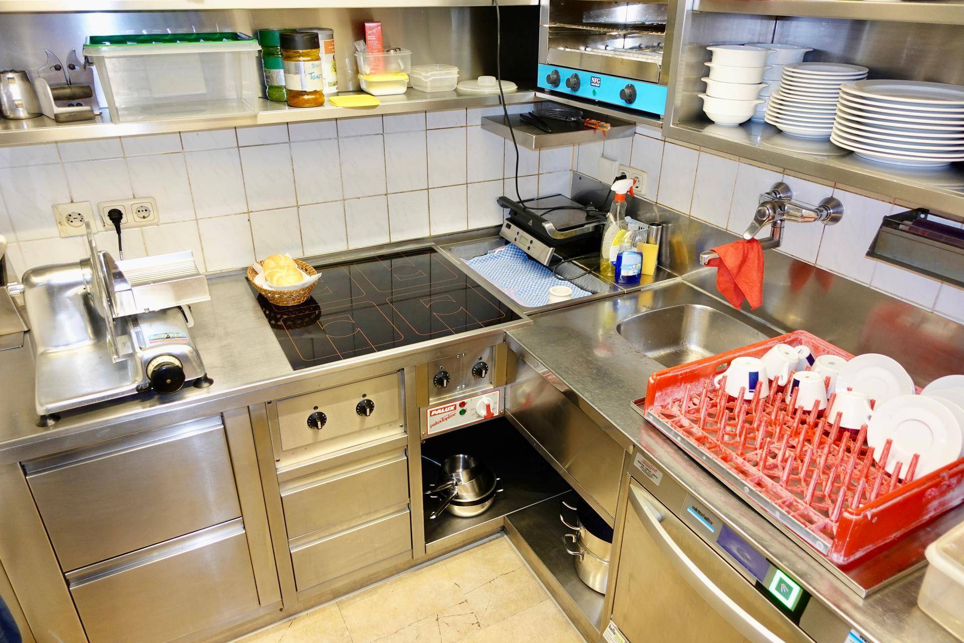 Eine professionelle Edelstahlküche mit Induktionskochfeld, Spülbecken und zahlreichen Arbeitsflächen für den Gastronomiebetrieb.