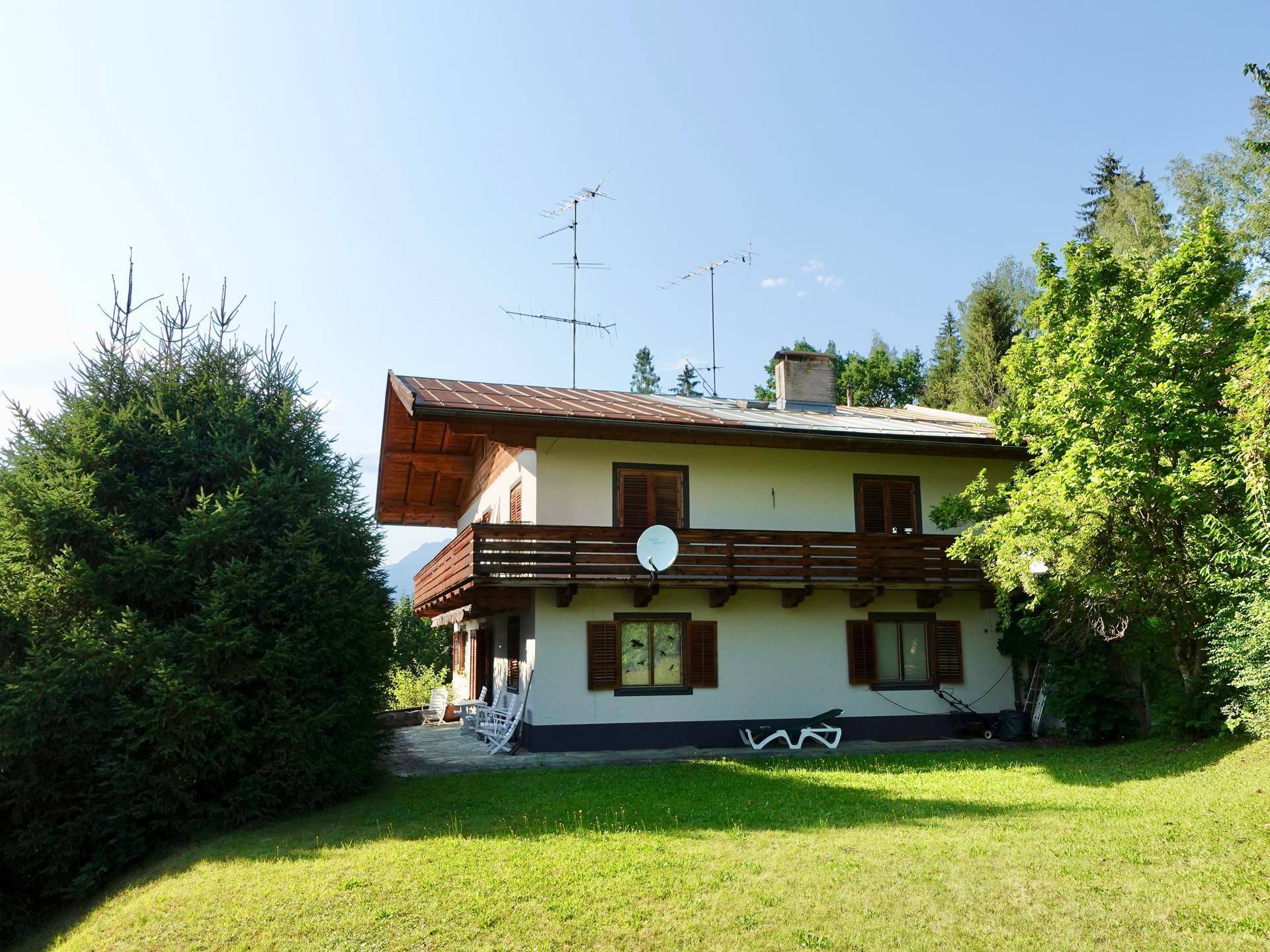 Freistehendes Haus mit Balkon und großem Rasenbereich unter blauem Himmel.