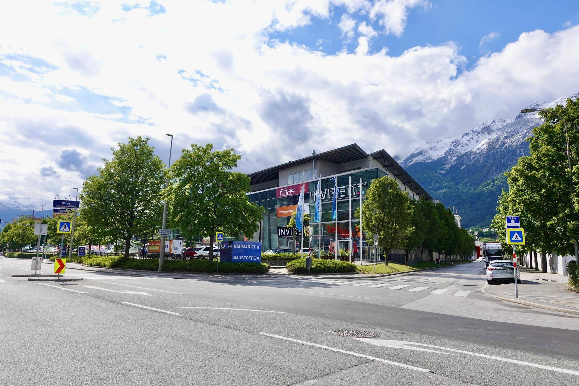 Weitläufige Außenansicht des modernen Geschäftsgebäudes von der Straße, umgeben von Bäumen und Bergen.