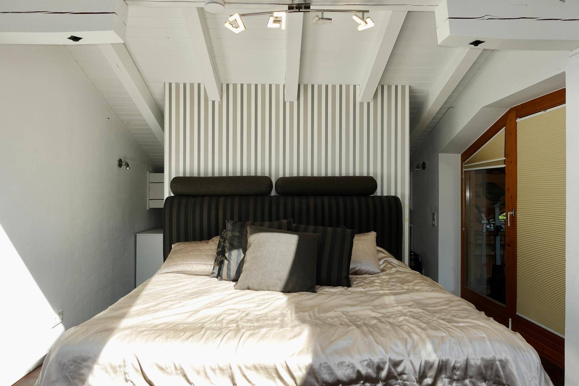 Gemütliches Schlafzimmer mit Doppelbett, Holzbalkendecke und gestreifter Tapete.