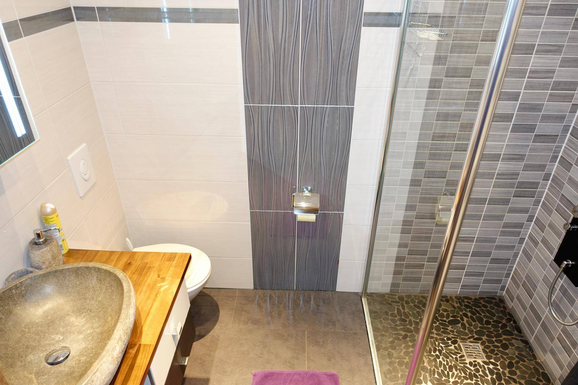 Modernes Badezimmer mit Steinsink, Duschkabine und grauen Fliesen.