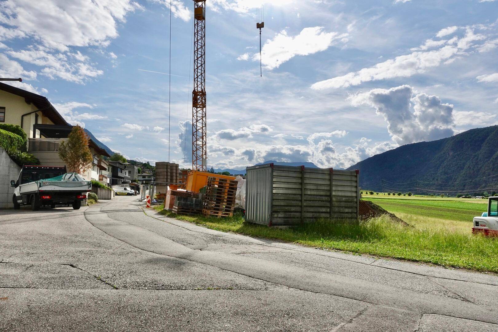 Zufahrtsstraße zu einer Baustelle mit Kran und Materiallager in bergiger Umgebung.