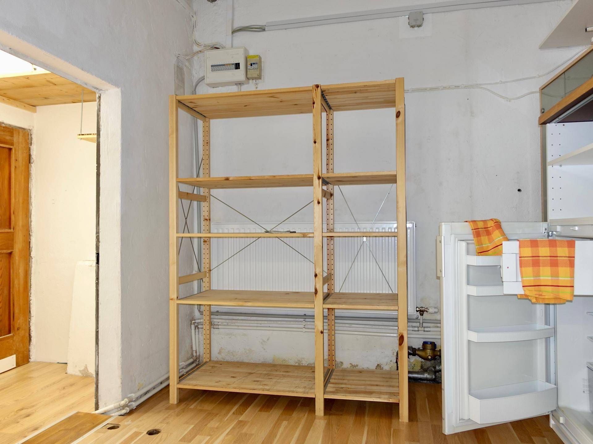 Praktischer Abstellraum mit Holzregalen, einem Kühlschrank und hellem Holzboden, ideal für Lagerzwecke.