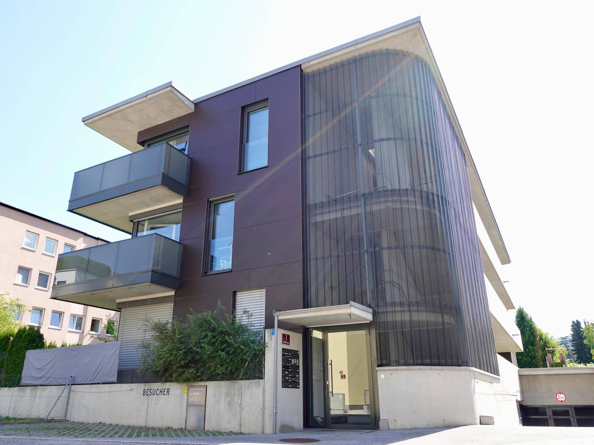 Modernes Wohngebäude mit dunkler Fassade, Balkonen und einer markanten gebogenen Glasfront.