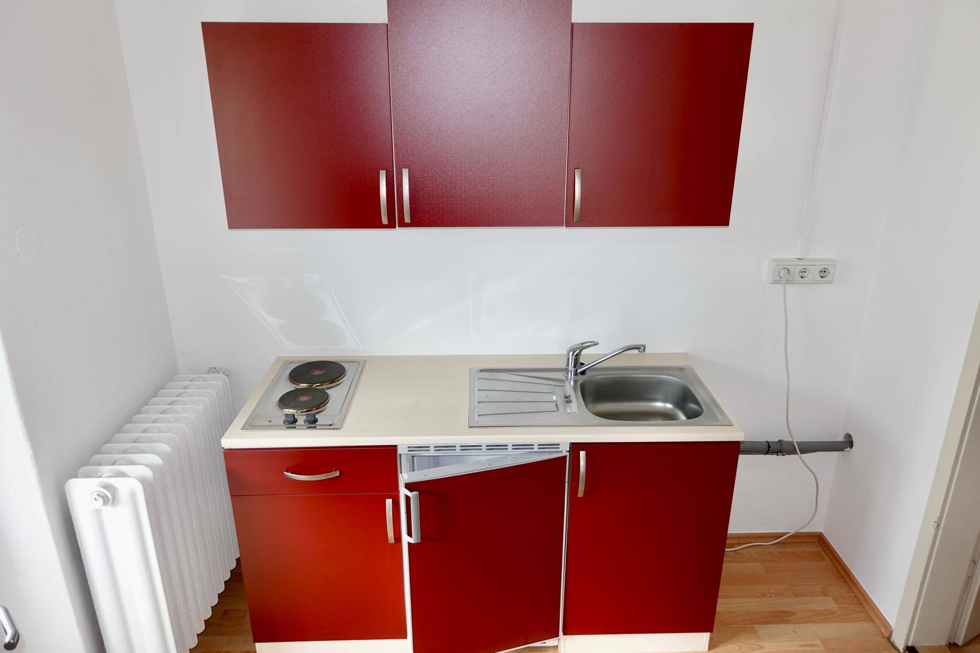Funktionale Küchenzeile mit roten Oberschränken, Spüle, Kochplatten und einem Heizkörper.