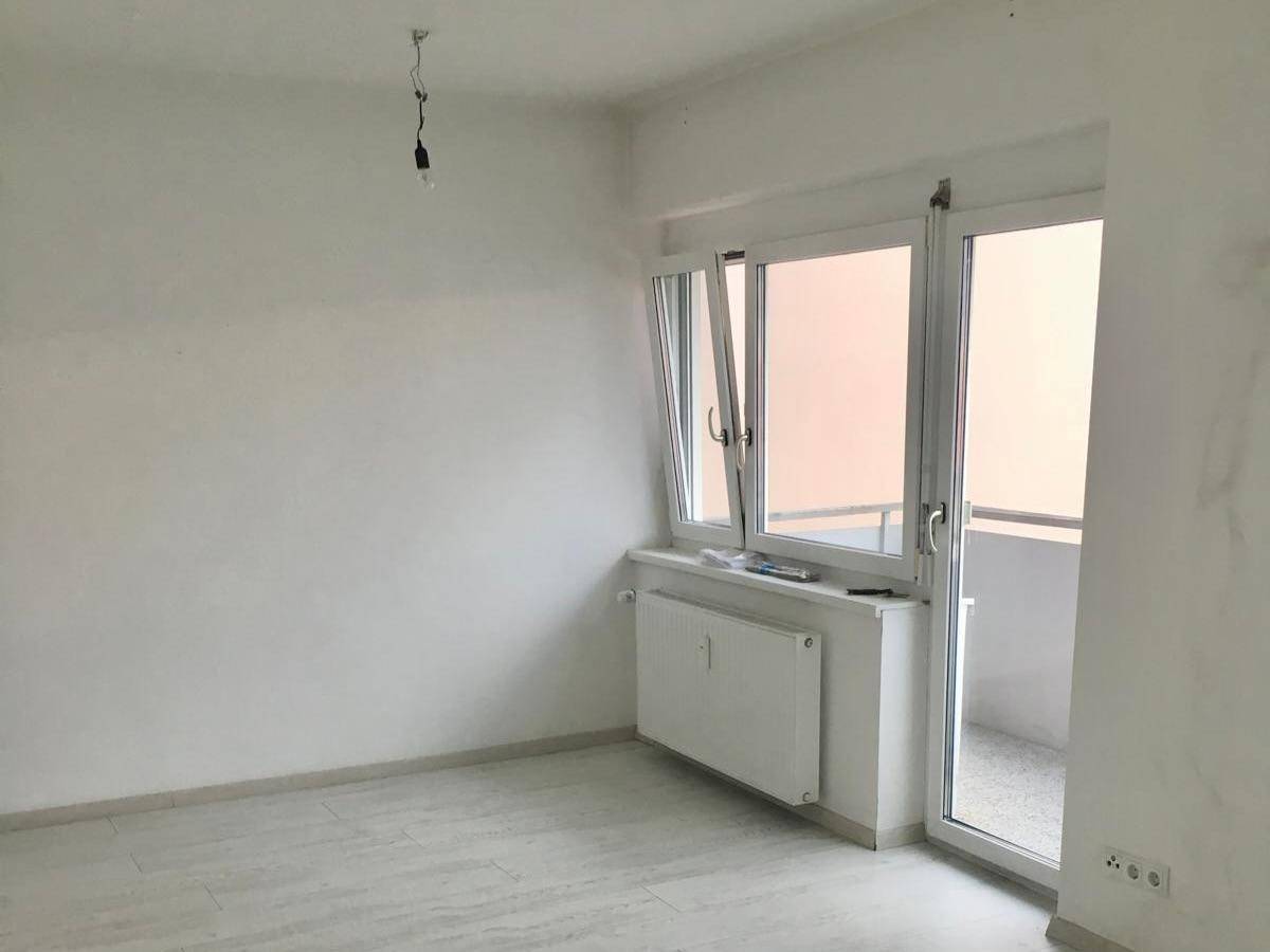 Lichtdurchfluteter Raum mit Fenster und Zugang zu einem kleinen Balkon, ausgestattet mit Heizkörper.