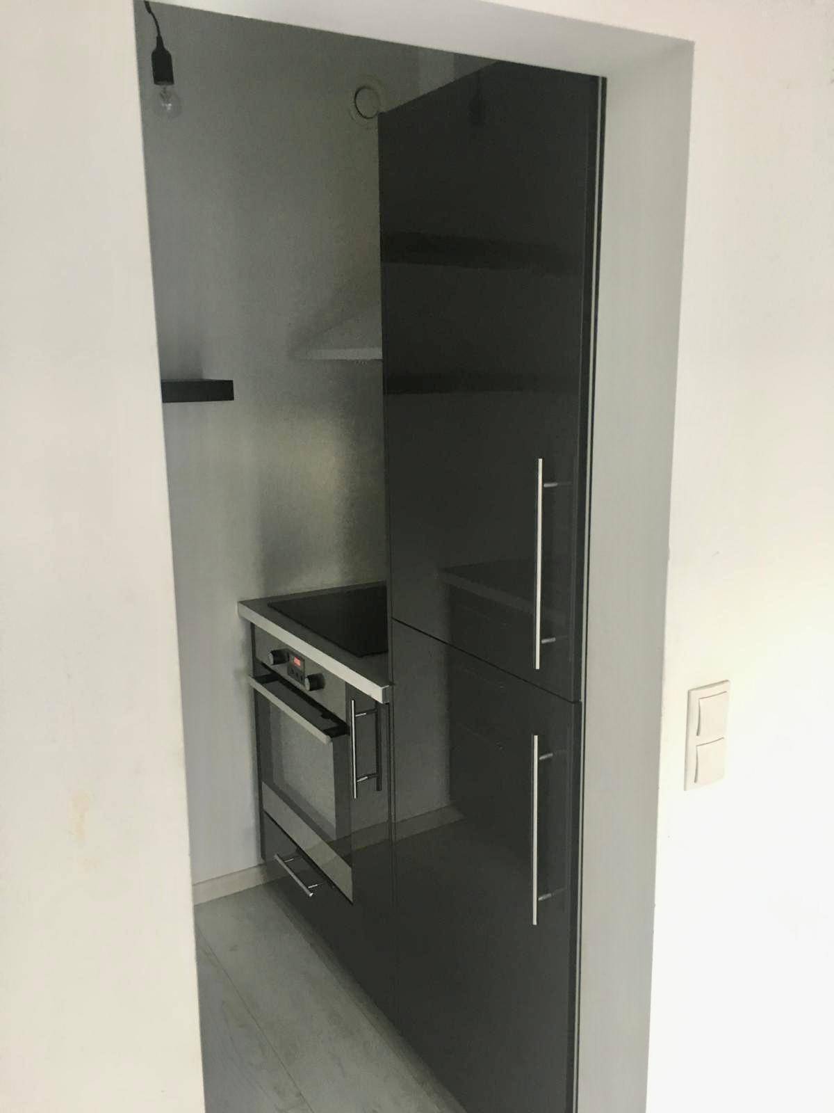 Kompakte Küchenzeile mit glänzenden schwarzen Schränken, integriertem Backofen und Spüle.