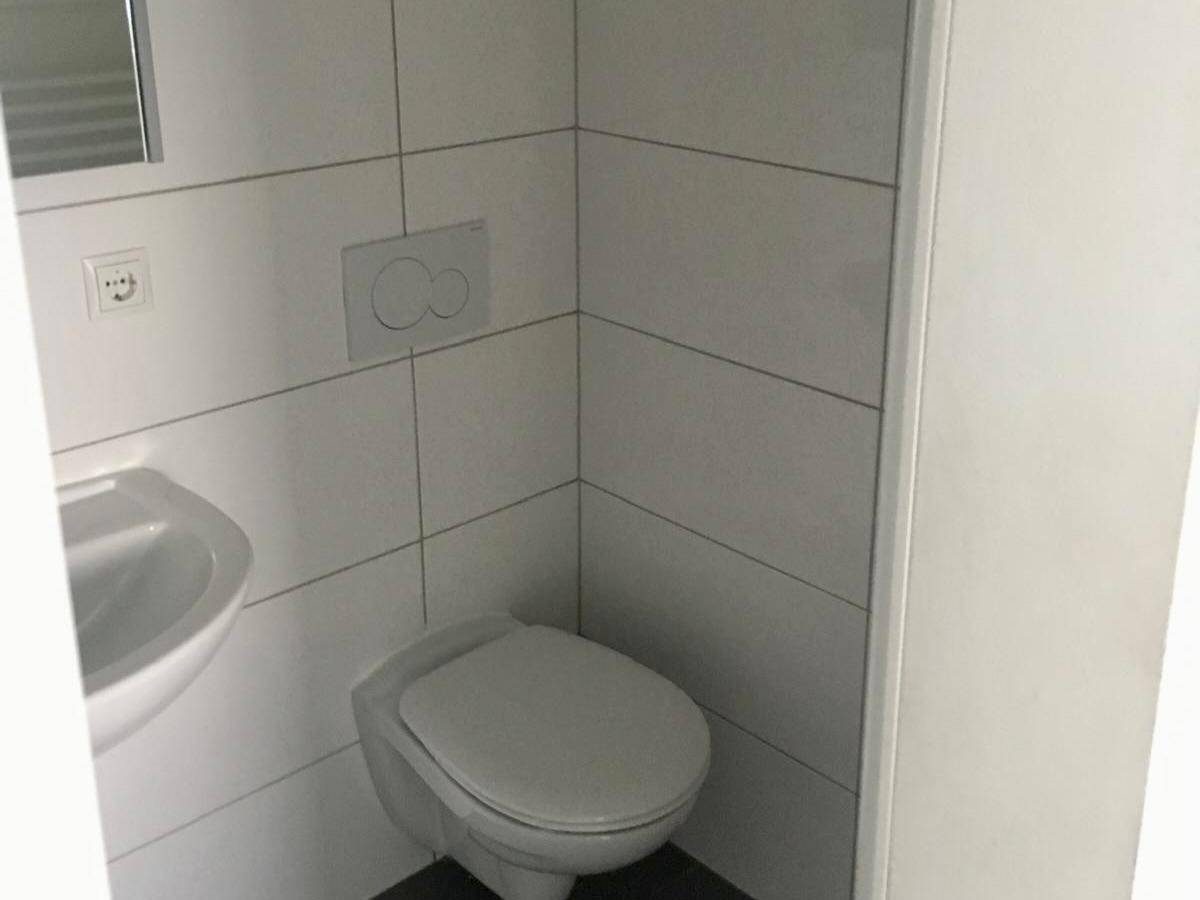 Kleines Badezimmer mit wandhängendem WC, Waschbecken und weißen Fliesen.