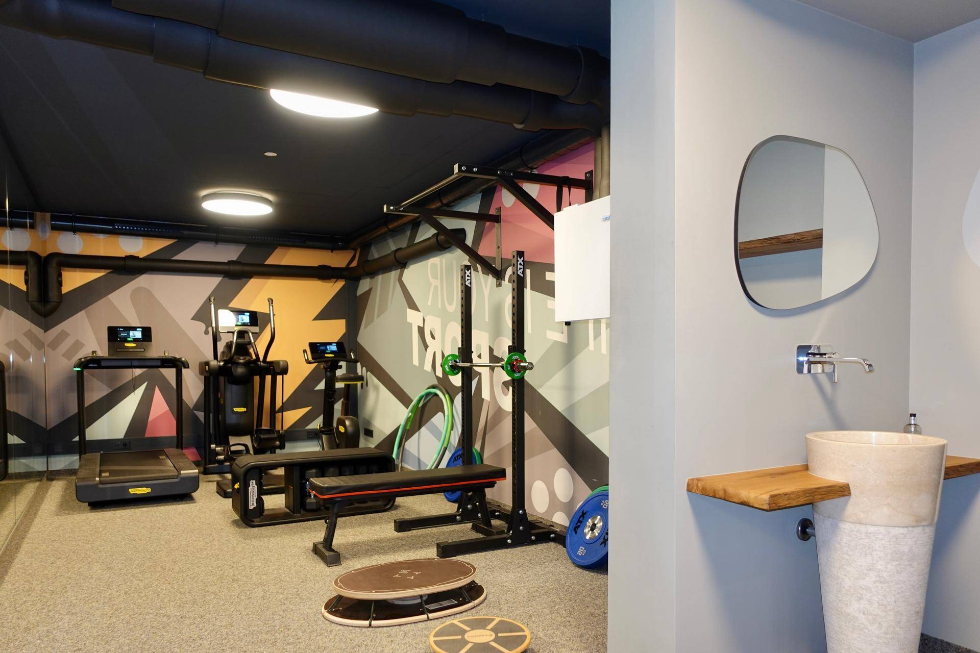 Moderner Fitnessraum mit verschiedenen Trainingsgeräten und Waschbeckenbereich.