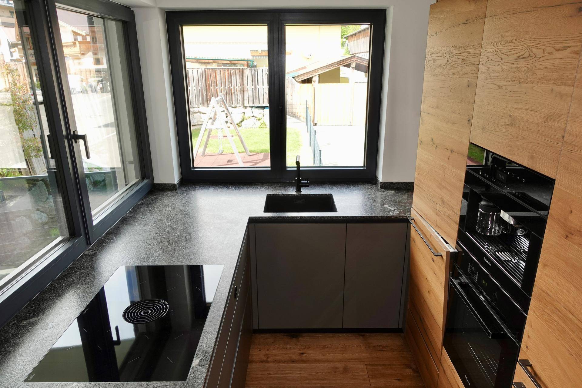 Moderne Küche mit Induktionskochfeld, Spüle und großem Fenster mit Blick ins Grüne.