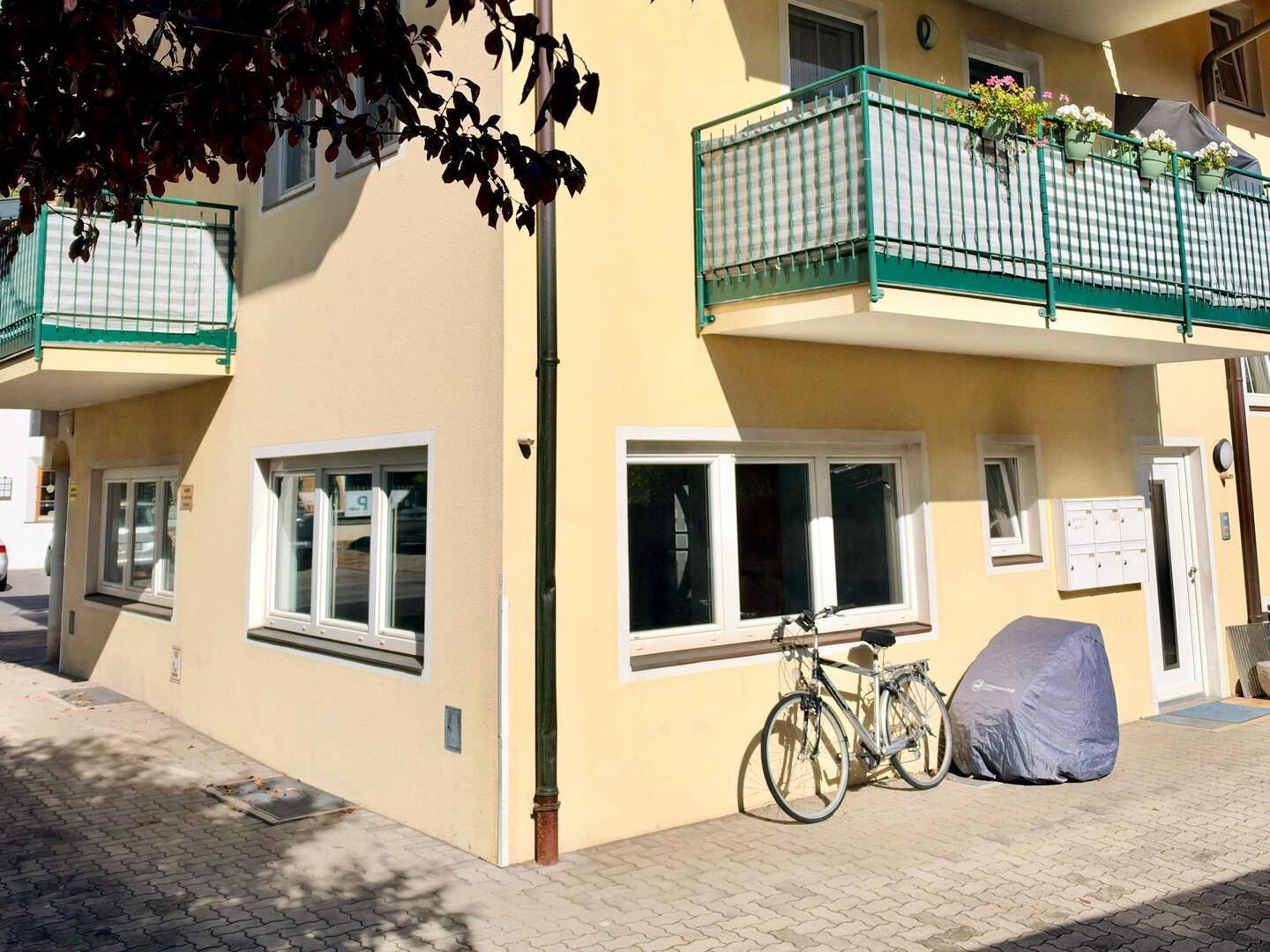 Ecke eines Gebäudes mit Balkonen und Fenstern, ein Fahrrad steht vor der Fassade.