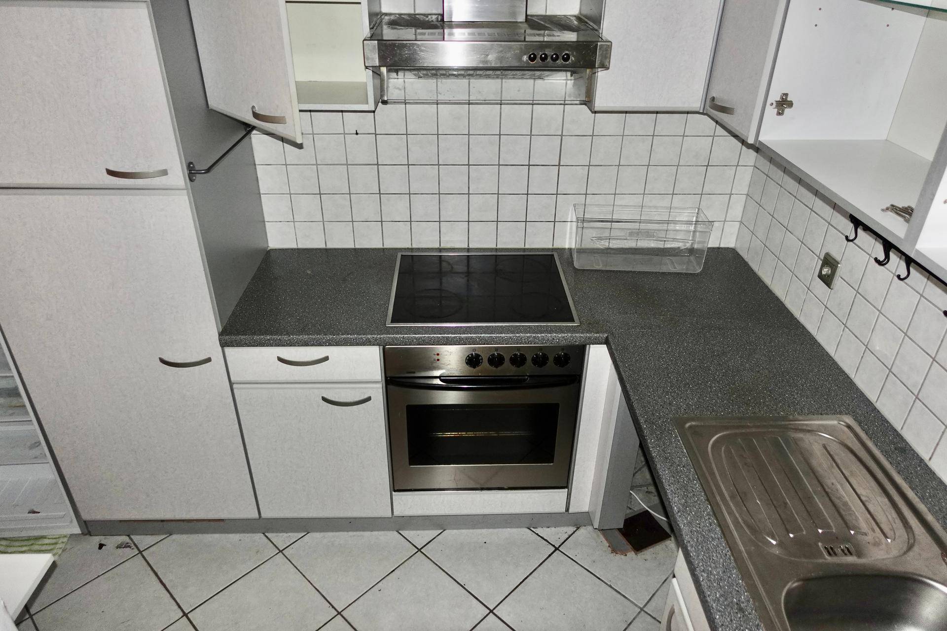Kleine Küche mit weißen Schränken, dunkler Arbeitsplatte und integriertem Herd.