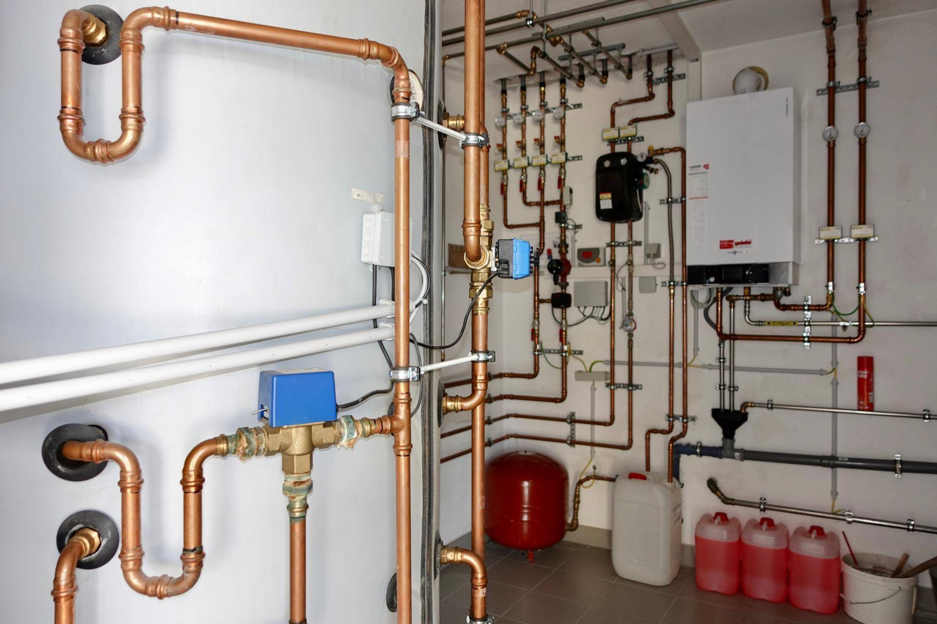 Heizungsraum mit komplexer Rohrinstallation und Warmwasserspeicher.
