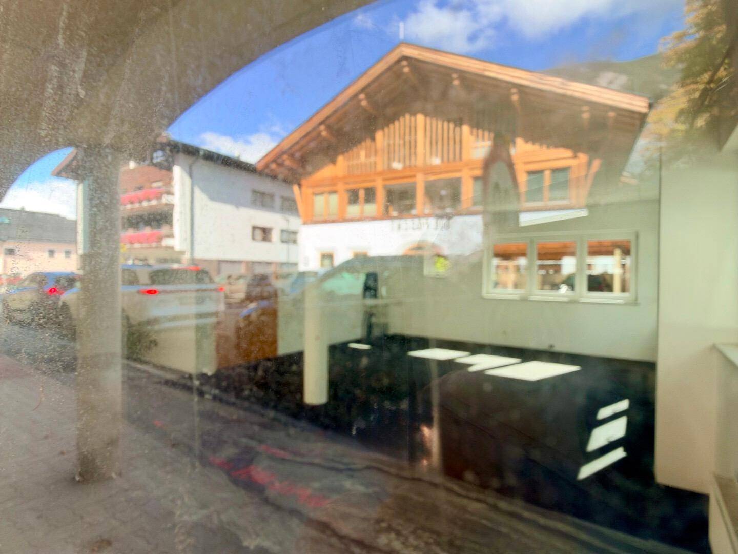 Blick durch ein Fenster mit Reflexionen, zeigt ein gegenüberliegendes Gebäude mit Holzbalkonen.