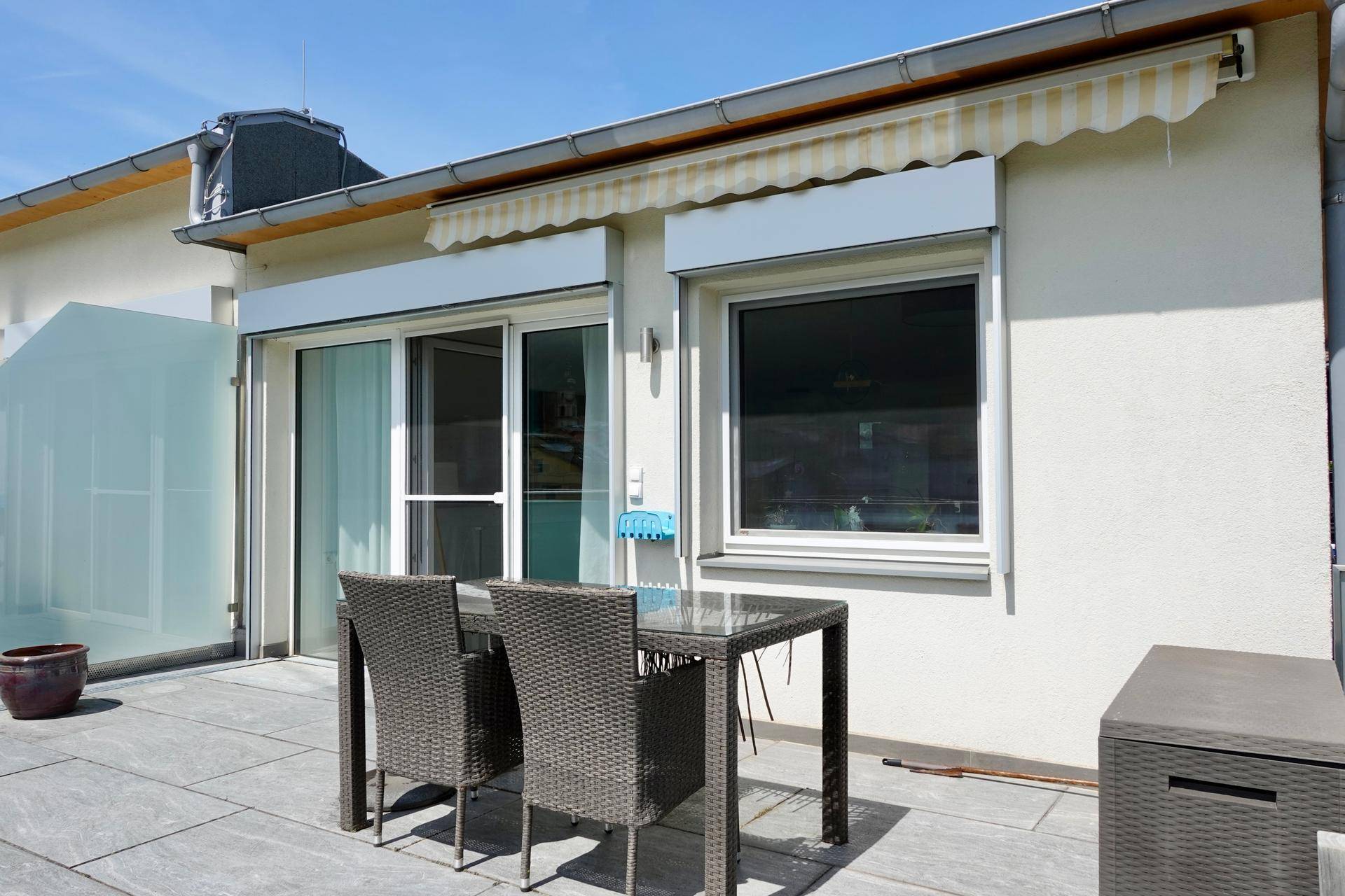 Geräumige Terrasse mit Gartenmöbeln, Sonnenmarkise und moderner Glasbrüstung.