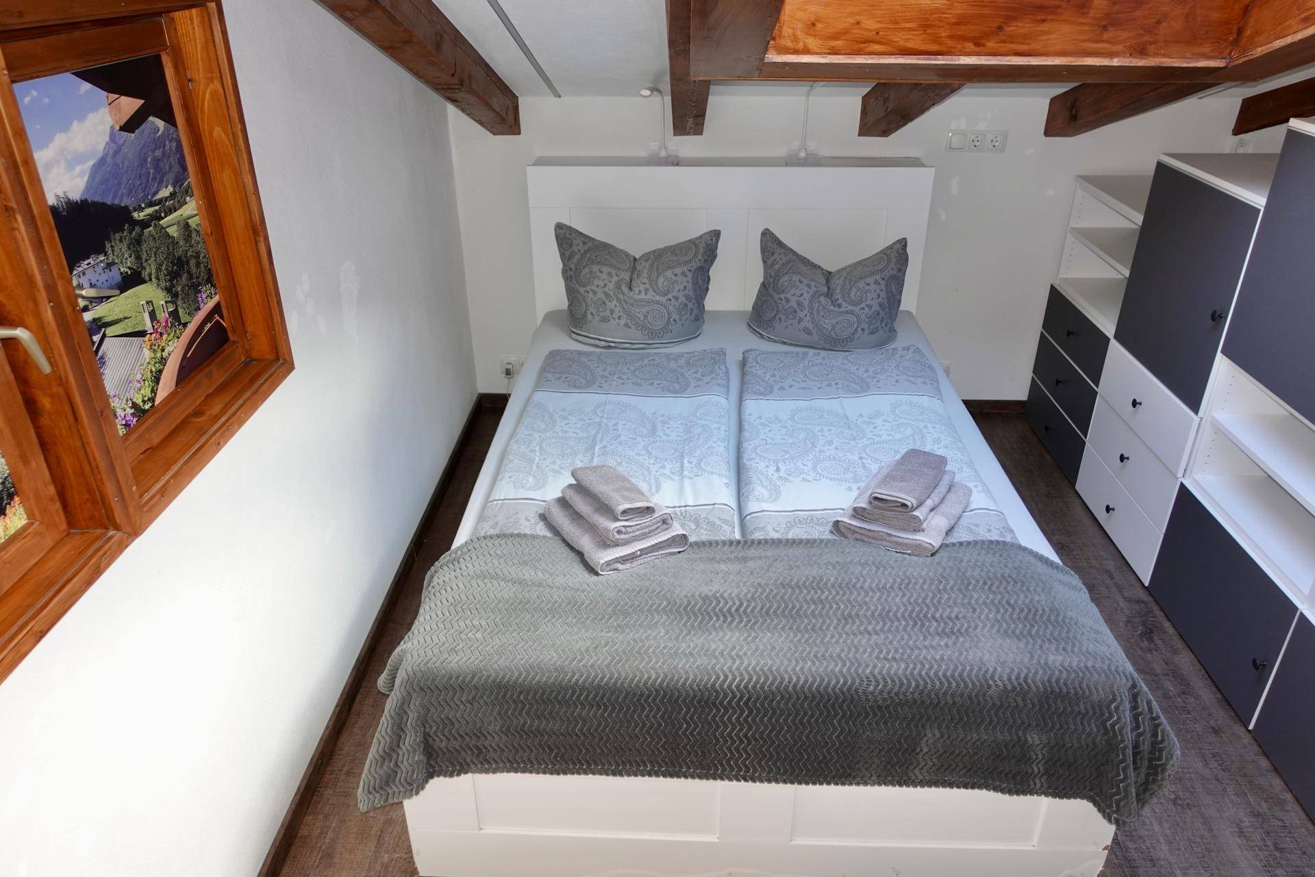 Gemütliches Schlafzimmer mit Holzbalken, Doppelbett und Blick auf die Berge.