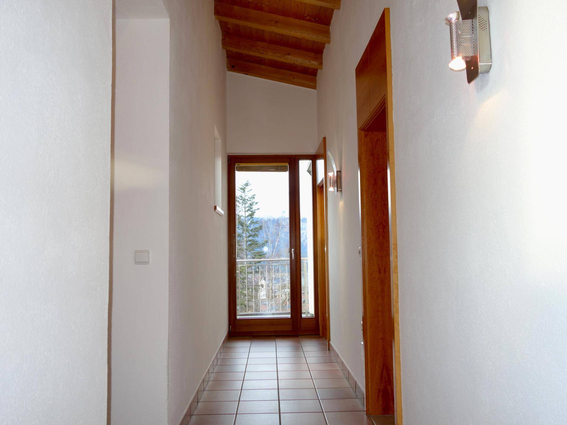 Heller Flur mit Fliesenboden, Holzdecke und Zugang zu einem kleinen Balkon.