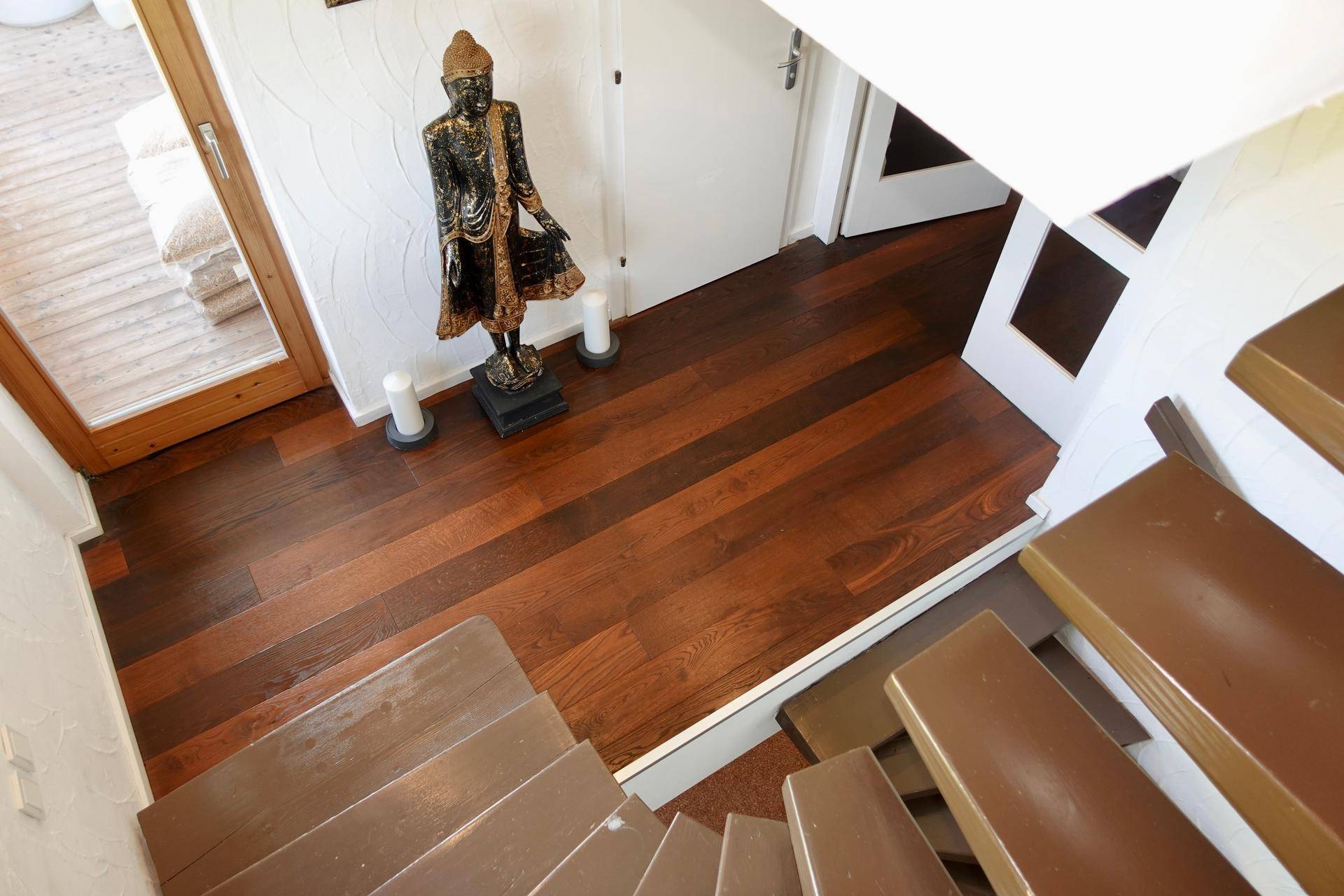 Heller Flur mit Holztreppe und dunklem Holzboden, dekoriert mit einer Buddha-Statue.