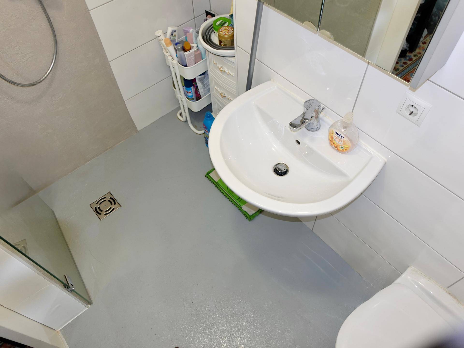 Funktionales Badezimmer mit Waschbecken, Spiegel und ebenerdiger Dusche.
