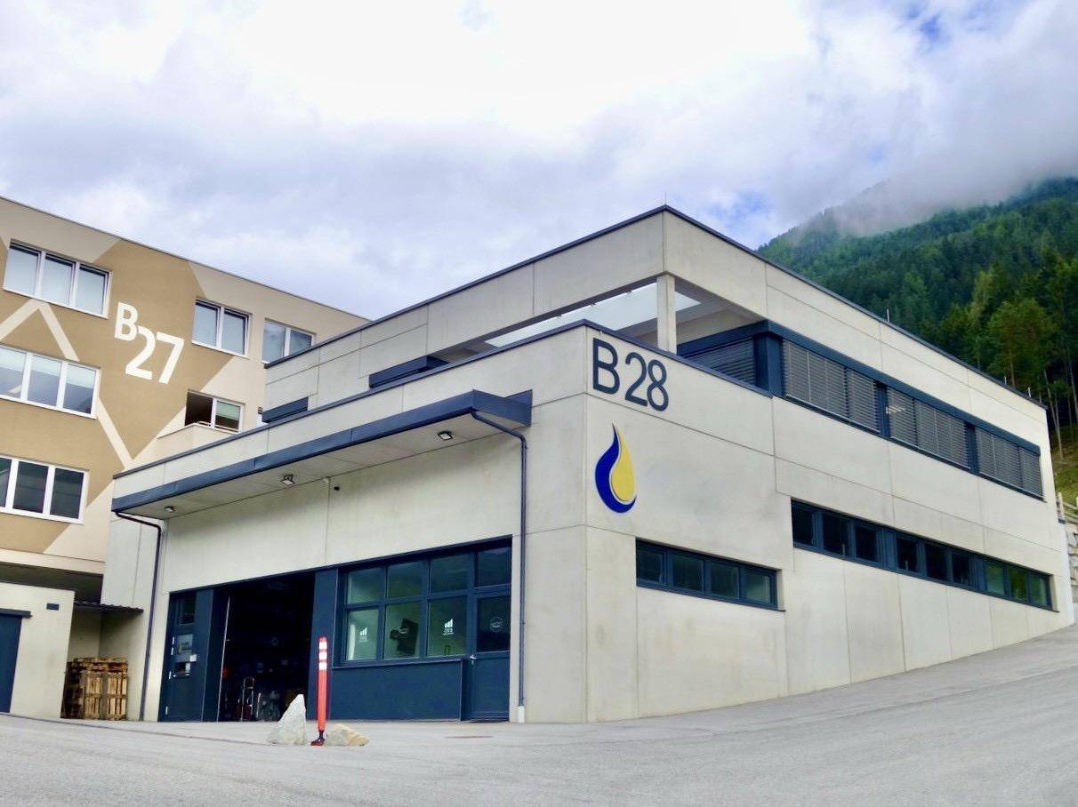 Modernes Geschäftsgebäude mit großer Garageneinfahrt und Fenstern, umgeben von einer Berglandschaft.