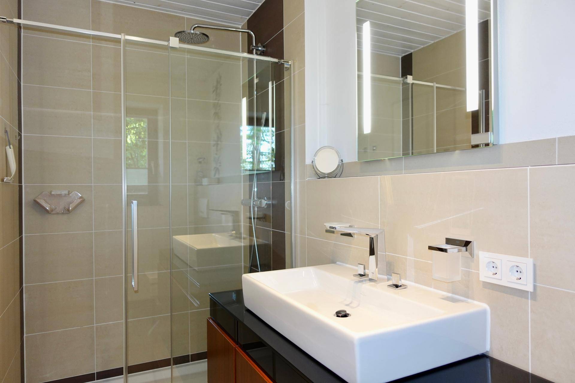 Modernes Badezimmer mit begehbarer Dusche, großem Waschbecken und hellen Fliesen.