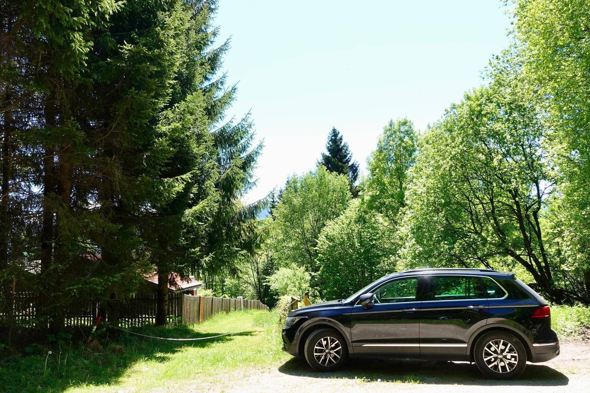Schwarzer SUV auf einem Schotterweg, umgeben von hohen Nadelbäumen und üppigem Grün.