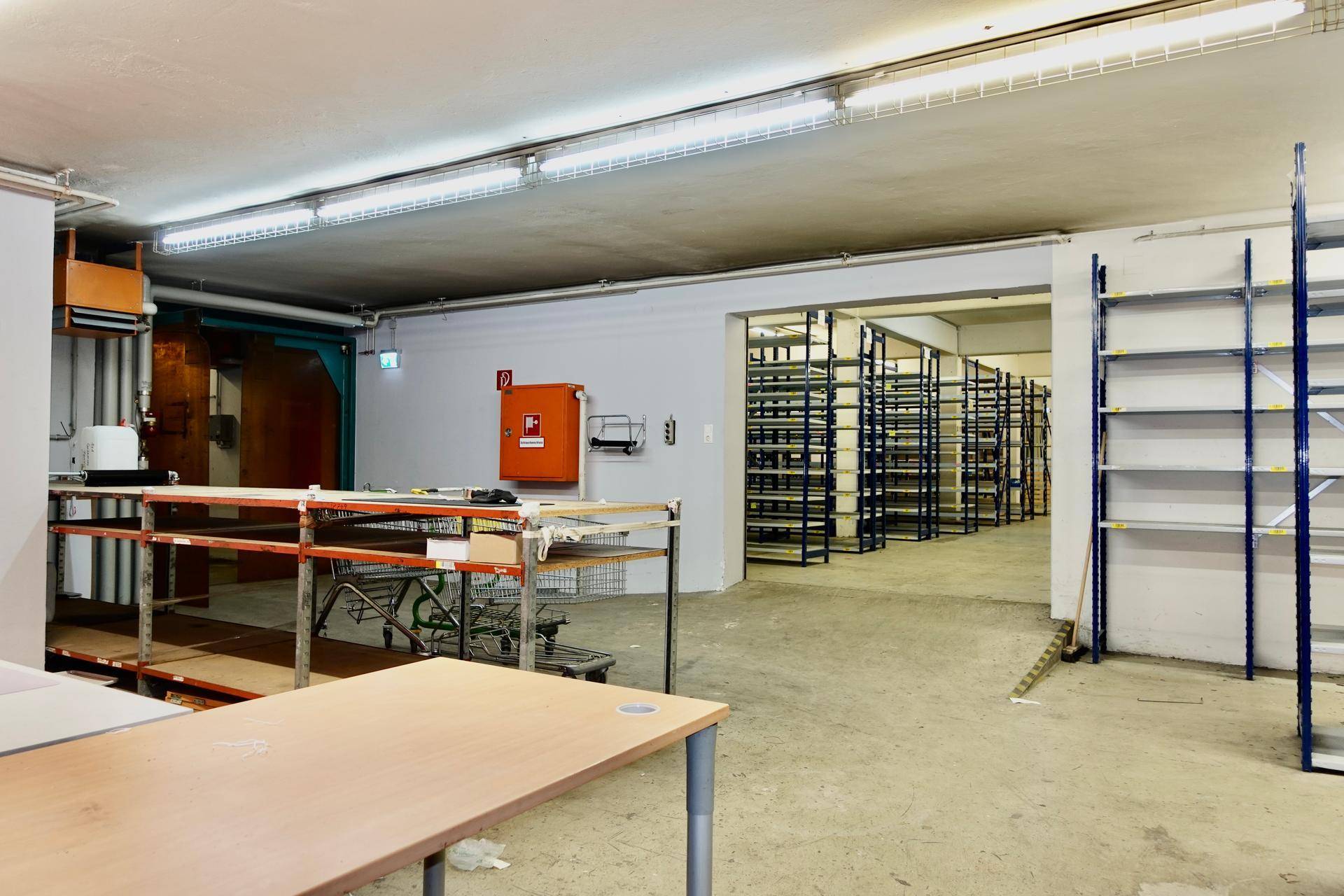 Lagerhalle mit leeren Regalen und einem Arbeitsbereich, beleuchtet von Neonröhren.
