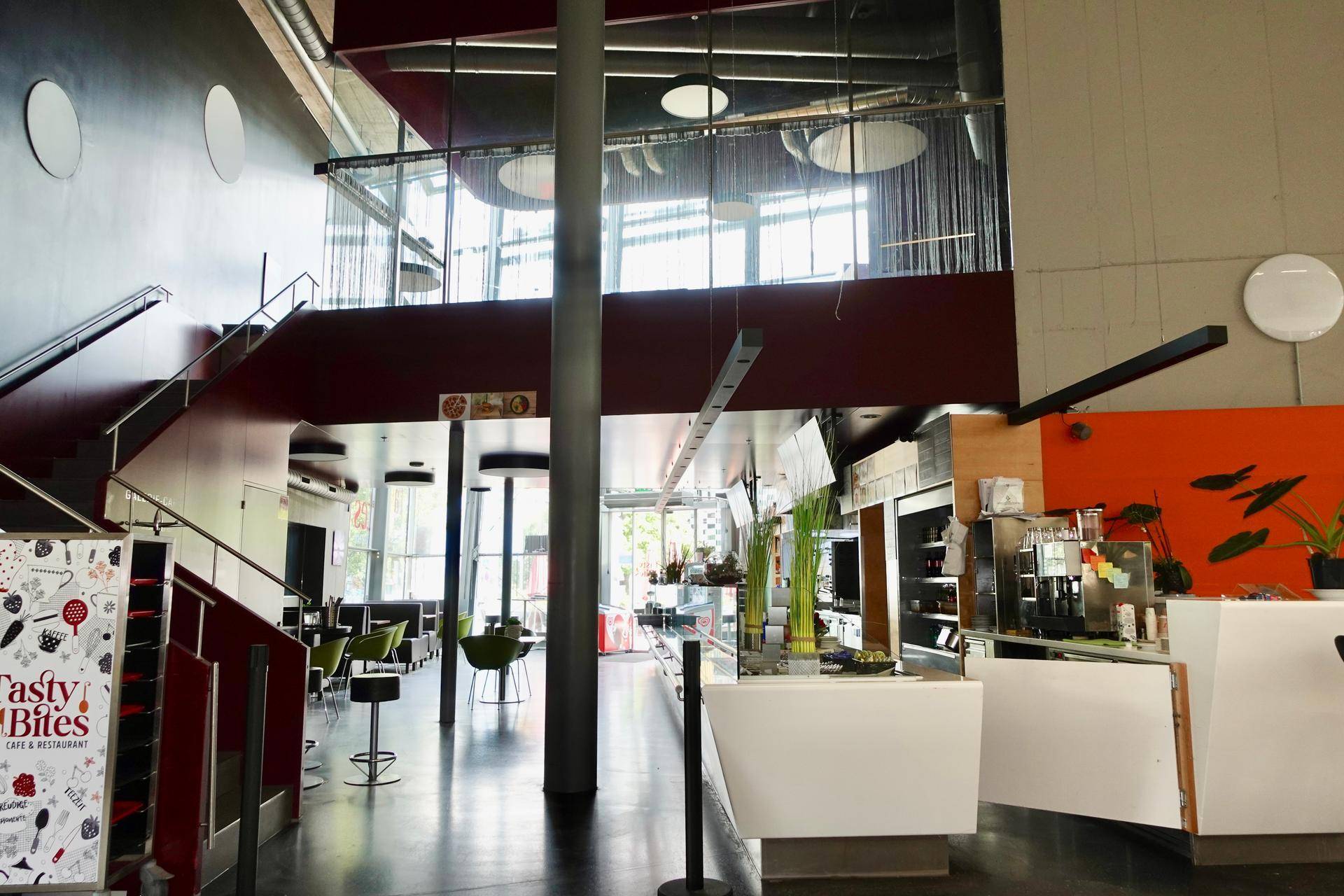 Eingangsbereich eines Restaurants mit Treppe zur oberen Etage, Theke und Sitzgelegenheiten.
