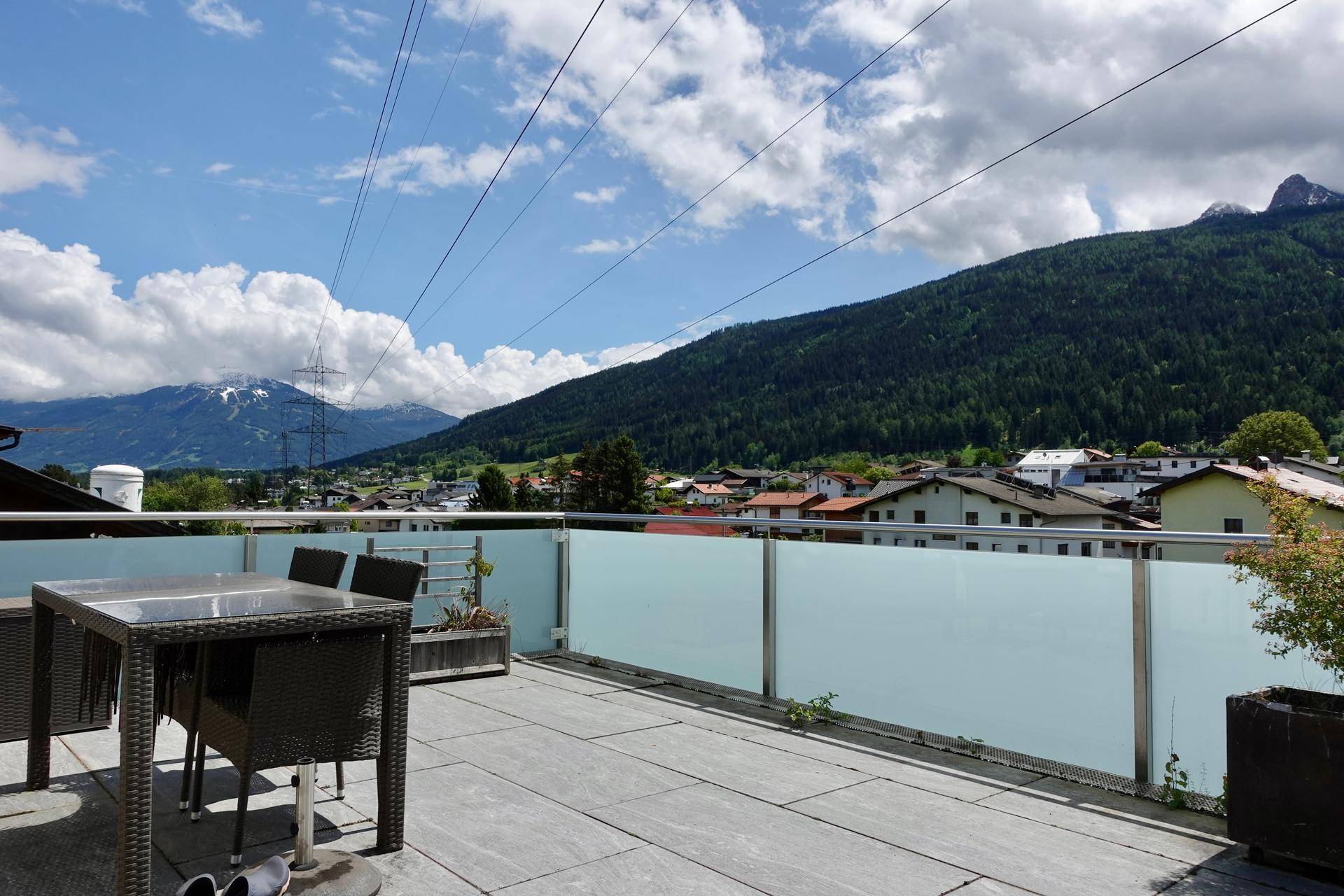 Sonnenterrasse mit Gartenmöbeln und weitem Panoramablick auf Berge und umliegendes Dorf.