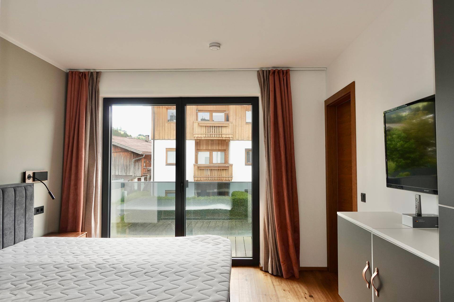 Schlafzimmer mit großem Bett, Zugang zum Balkon und Blick auf gegenüberliegende Gebäude.
