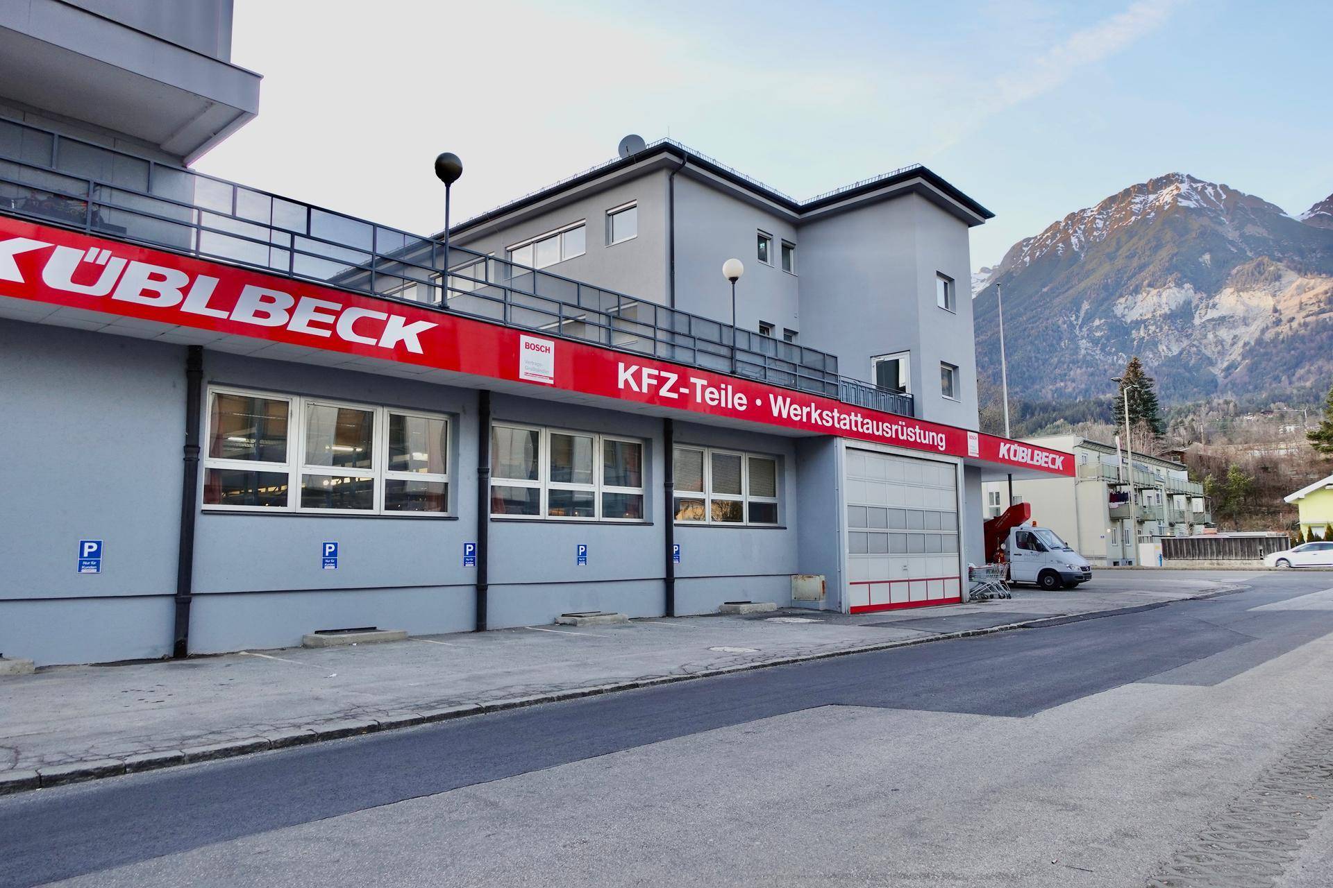 Geschäftsgebäude mit Beschilderung für KFZ-Teile und Werkstattausrüstung, umgeben von Bergen.