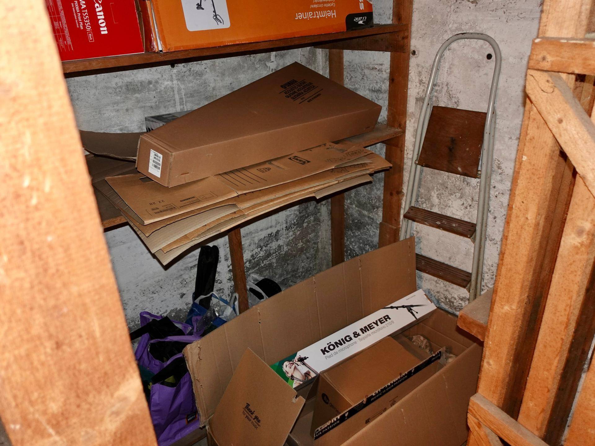Unaufgeräumter Abstellraum im Keller mit Holzregalen und verschiedenen Kartons.