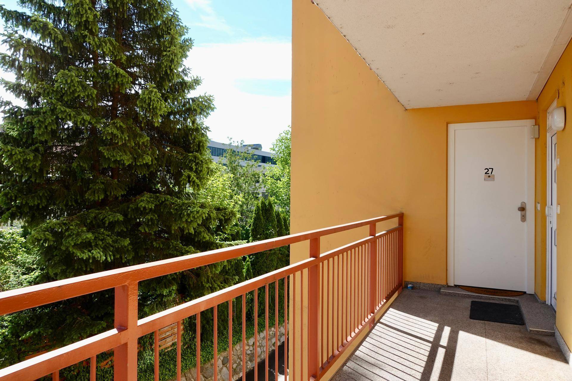 Balkon mit orangefarbenem Geländer und Blick ins Grüne, Zugang zur Wohnung.