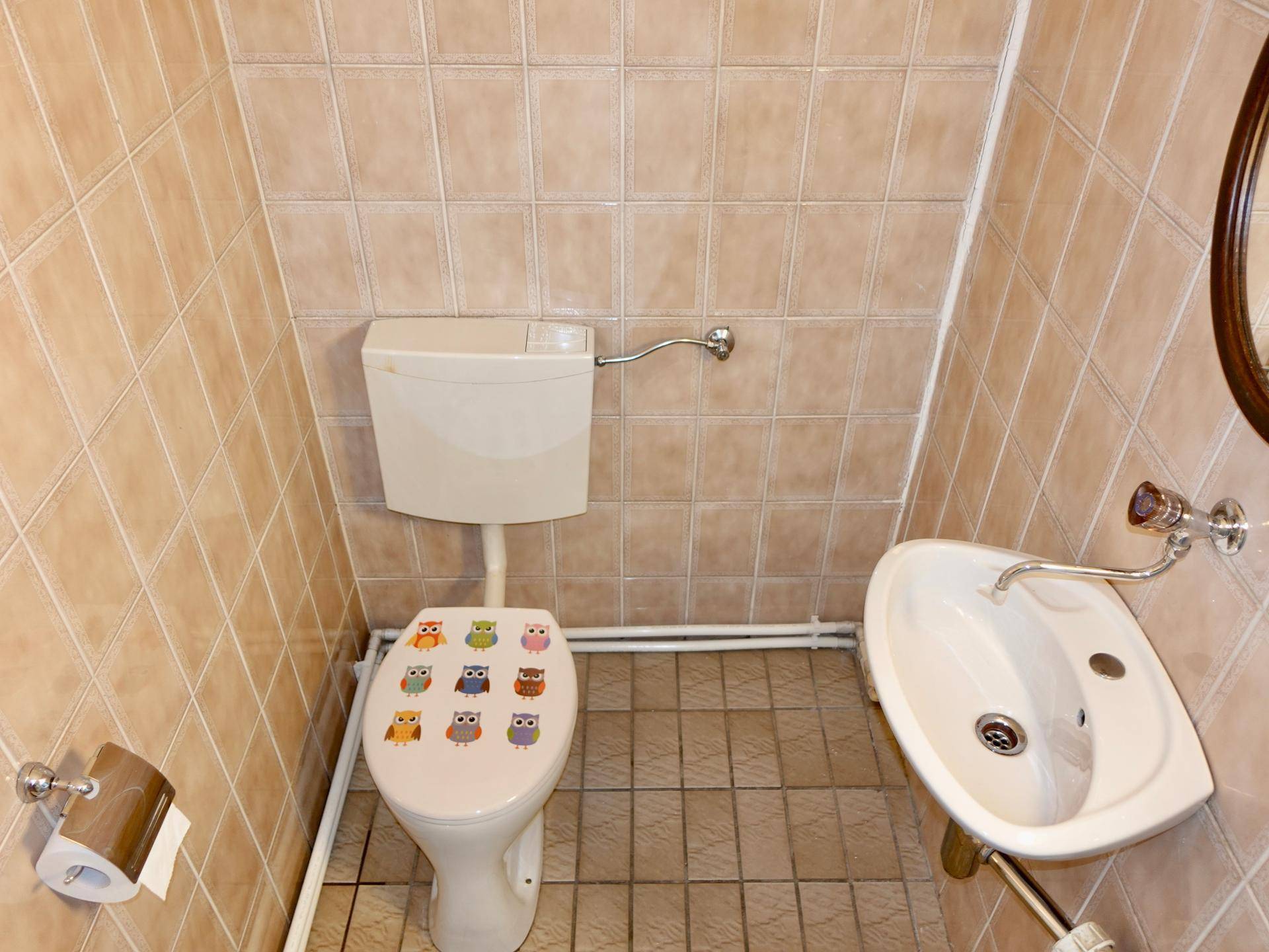 Kleines Gäste-WC mit beigefarbenen Fliesen, einer Toilette mit verspieltem Sitz und einem kompakten Waschbecken.