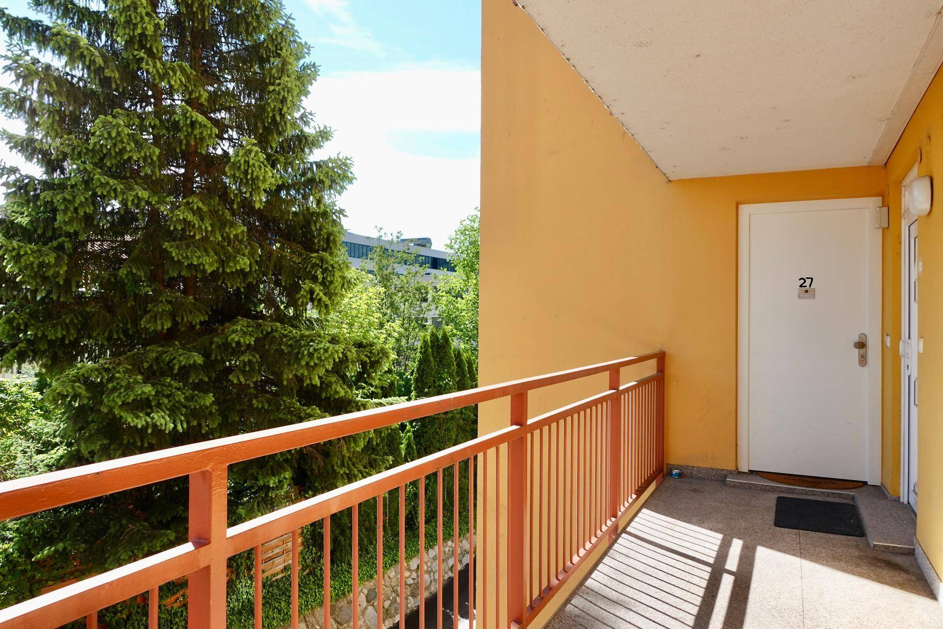 Balkon mit orangefarbenem Geländer und Blick ins Grüne, Zugang zur Wohnung.