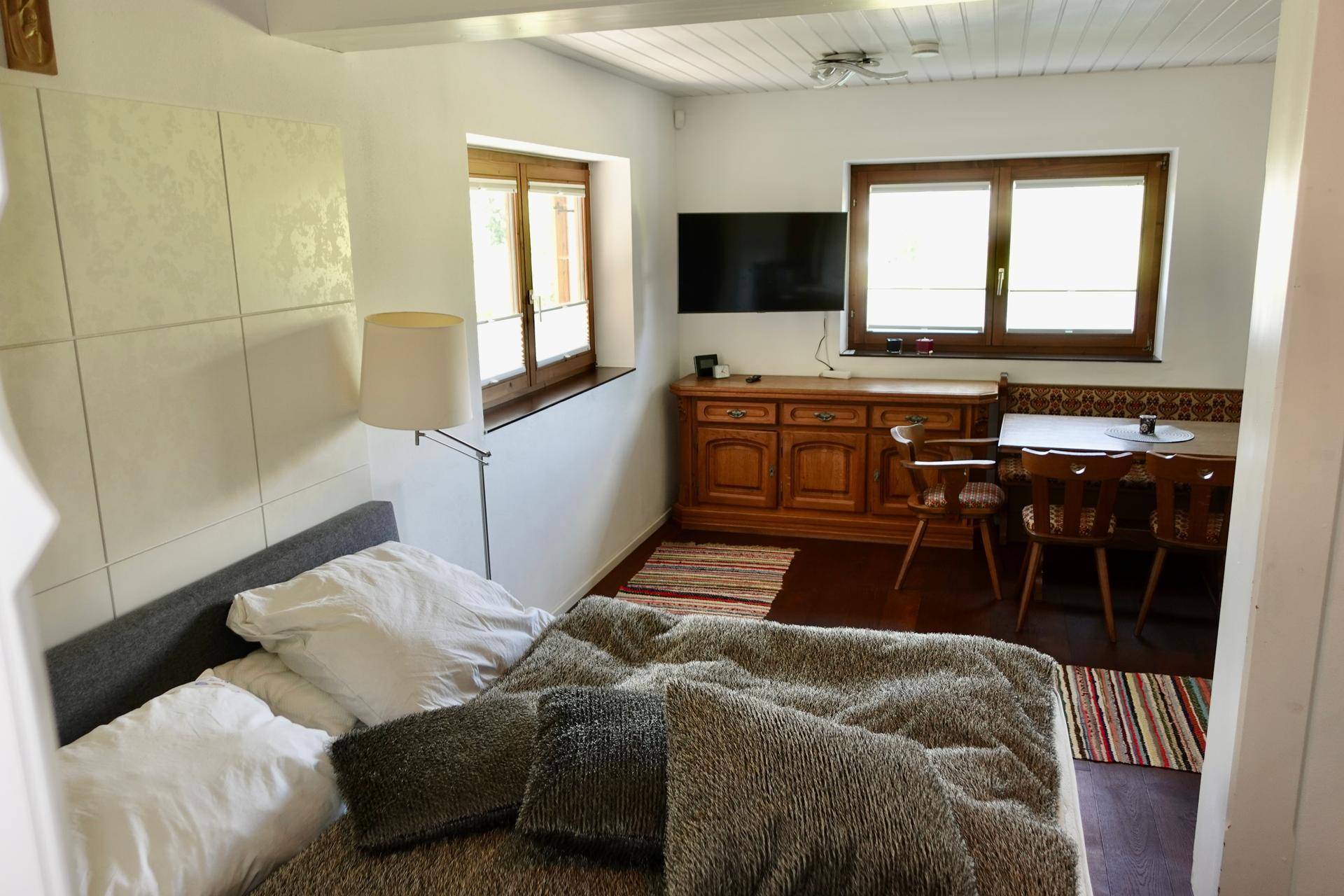 Schlafzimmer mit Doppelbett, Esstisch und Fernseher, hell durch große Fenster.