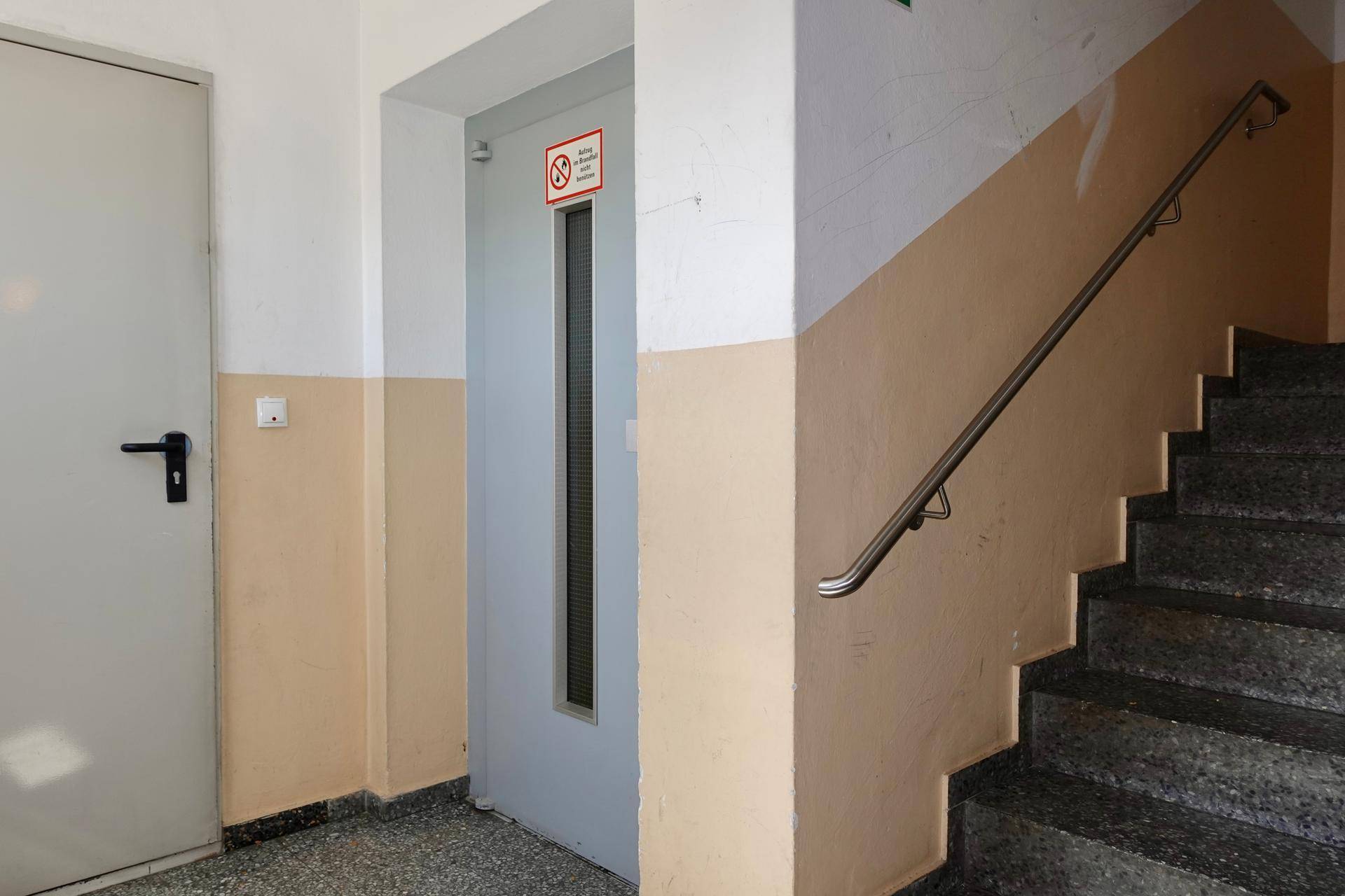 Treppenhaus mit Granitstufen und Handlauf neben einem Aufzug in einem Mehrfamilienhaus.