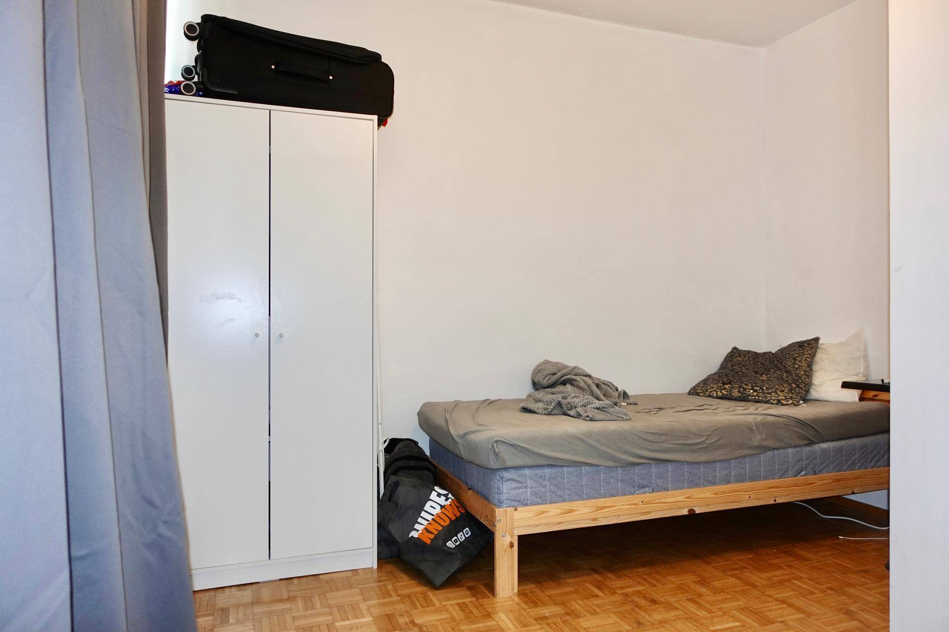 Schlafzimmer mit Einzelbett, weißem Kleiderschrank und Parkettboden.
