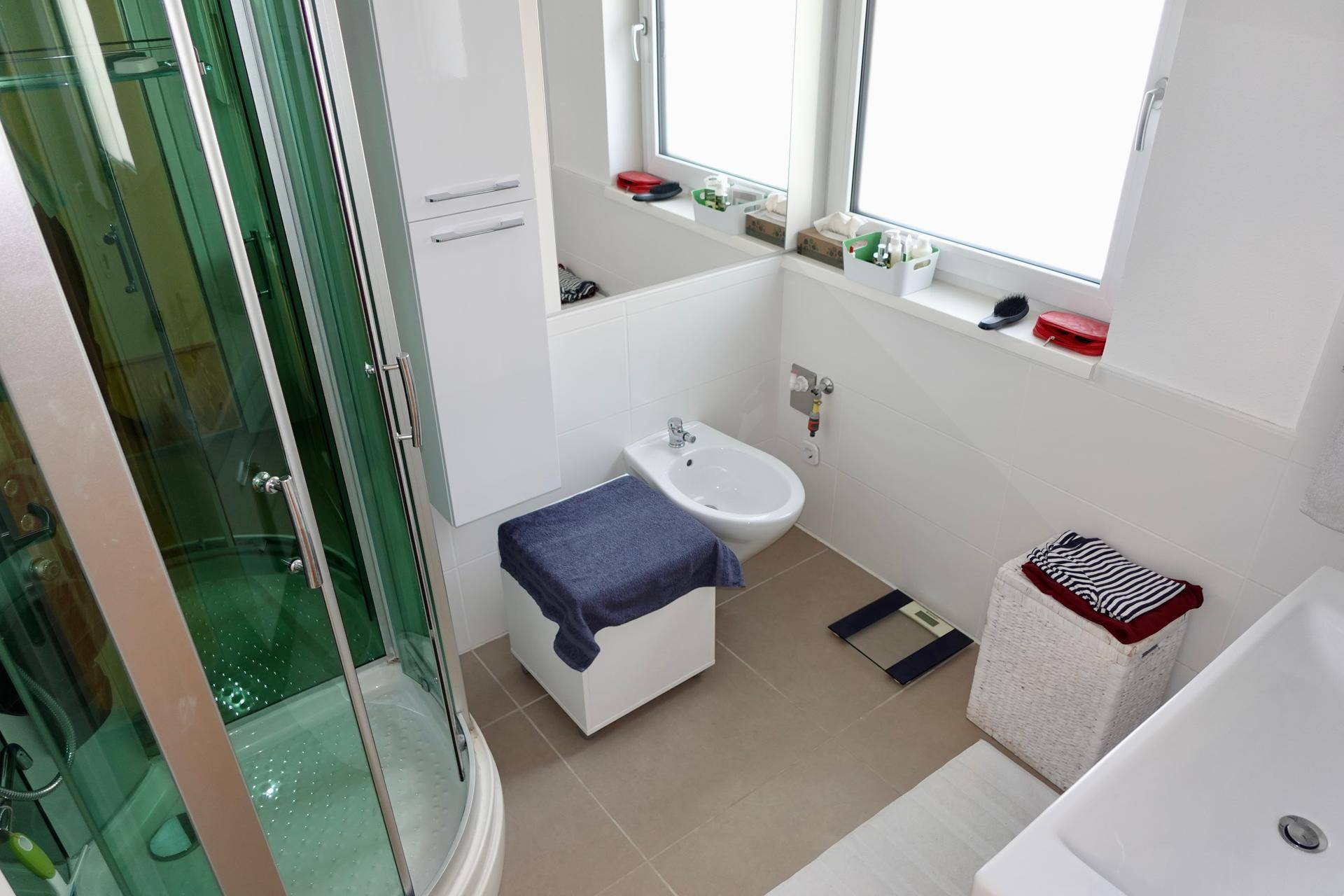 Helles Badezimmer mit Duschkabine, Bidet, Waschbecken und großem Fenster für Tageslicht.