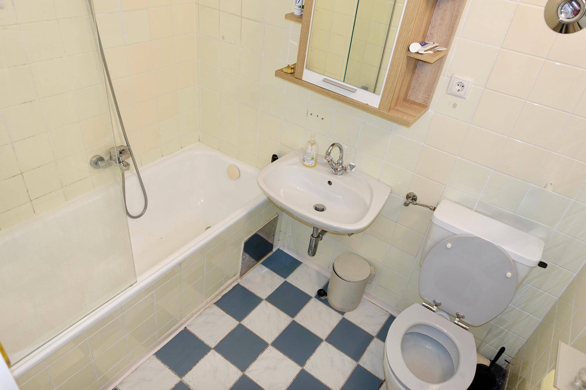 Badezimmer mit Badewanne, Waschbecken und WC, ausgestattet mit gelben und karierten Fliesen.