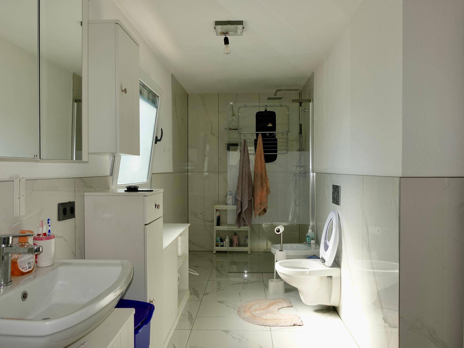 Modernes Badezimmer mit Dusche, WC, Waschbecken und hellen Fliesen.