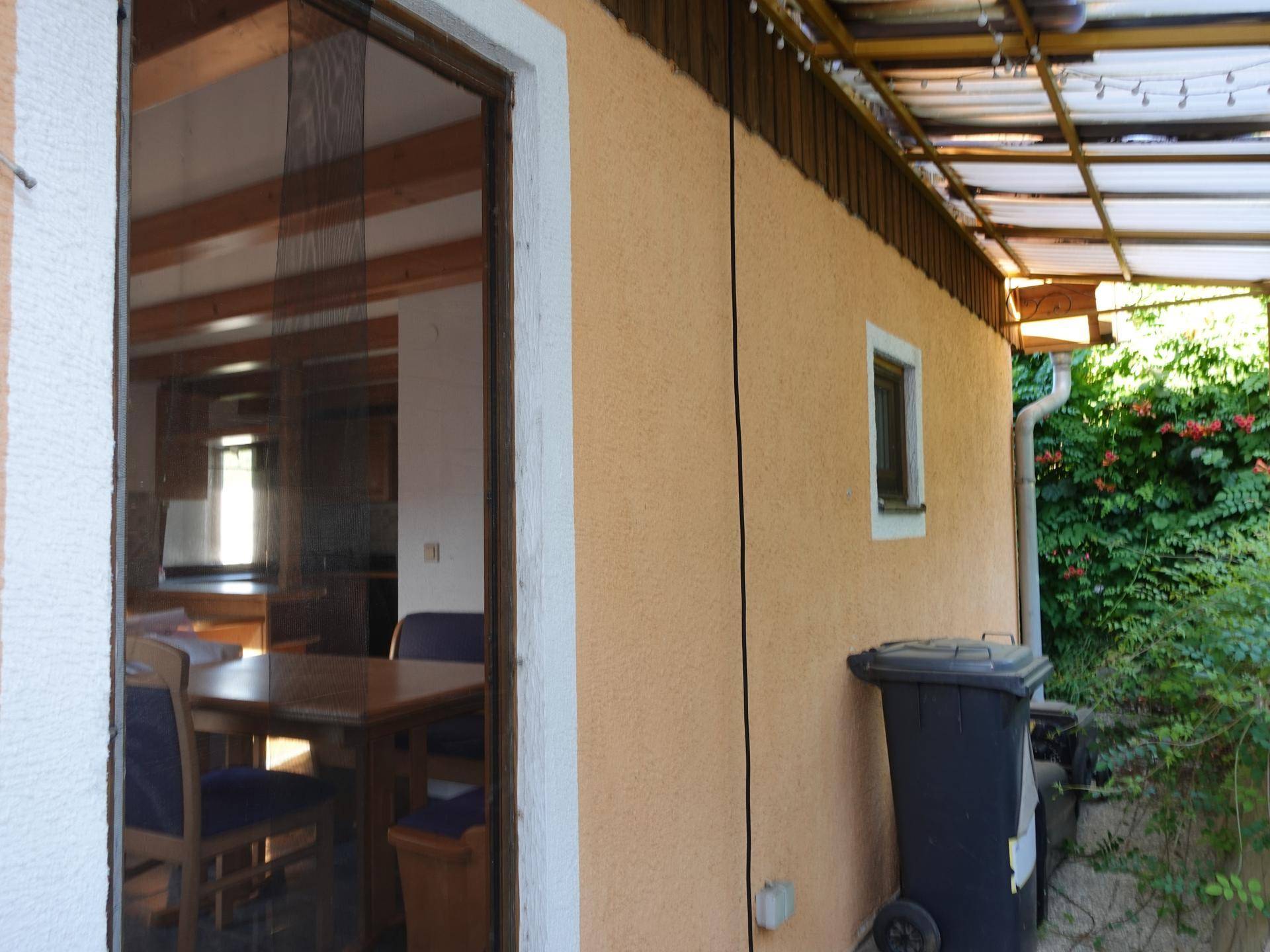 Seitenansicht des Hauses mit überdachtem Bereich und Mülltonne.