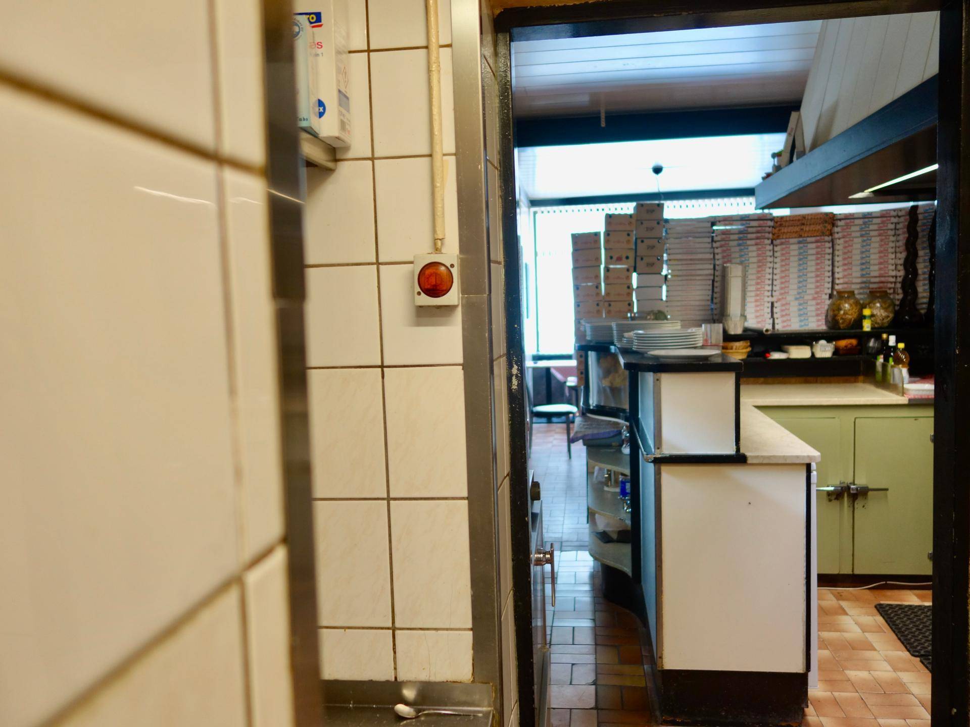 Blick aus der Küche in den Restaurantbereich, mit gestapelten Pizzakartons und Geschirr.