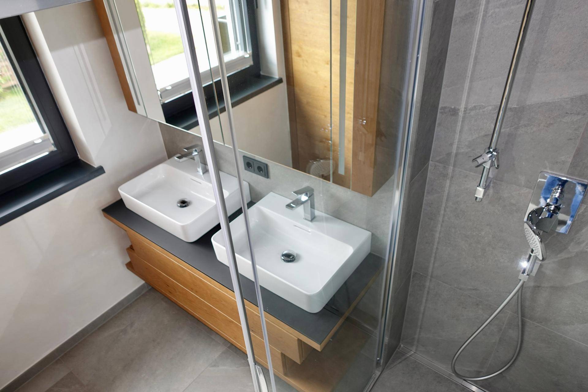 Modernes Badezimmer mit Doppelwaschbecken, Dusche und Fenster für Tageslicht.