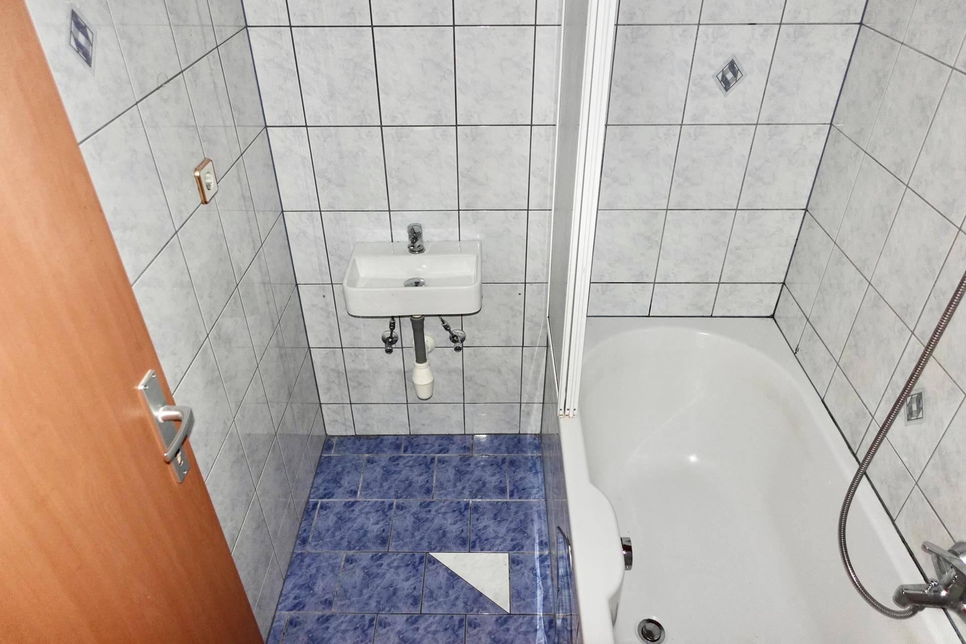 Kleines Badezimmer mit blauen Fliesen, Badewanne und einem kleinen Waschbecken.